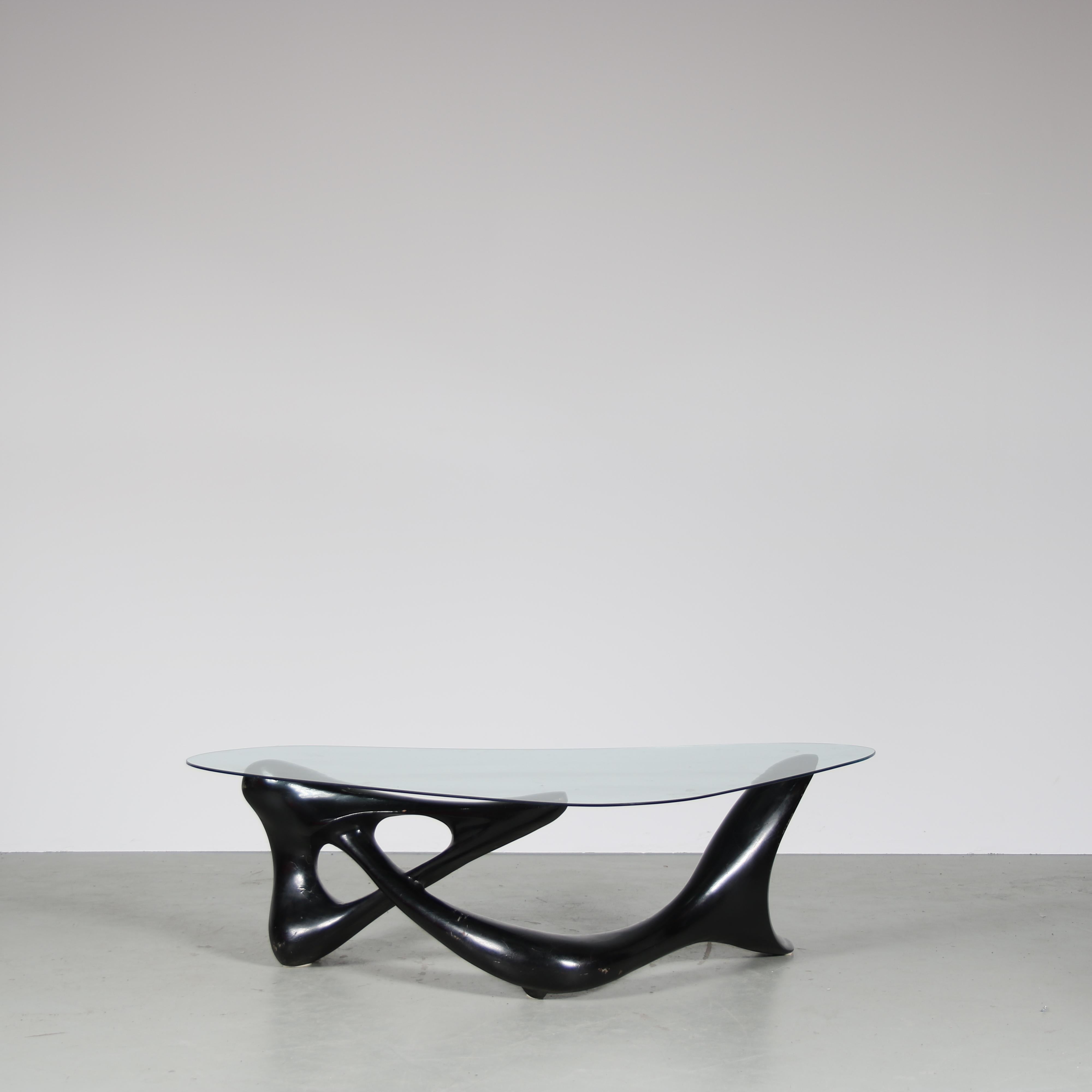 A striking coffee table from Italy, manufactured in the 1950s.

Its organic-shaped black wooden base with elegant curves and angles contrasts beautifully with the freeform glass top, creating a unique and eye-catching piece. The table’s minimalist