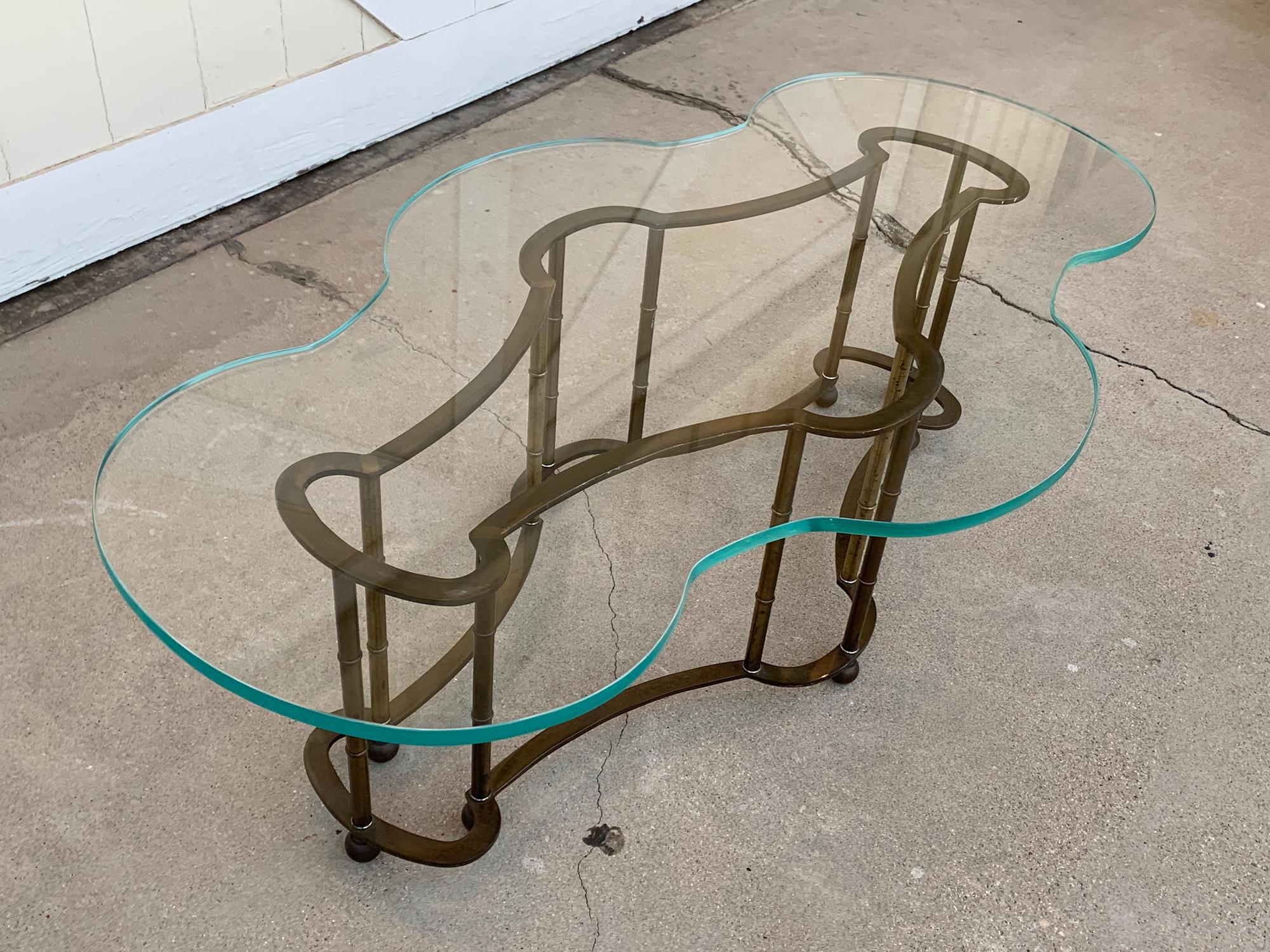 Freeform coffee table in brass and glass designed and manufactured by Mastercraft.
The table has beautiful freeform shaped with matching glass, the brass base has a beautiful antique patina and the glass has a beautiful water edged and freeform