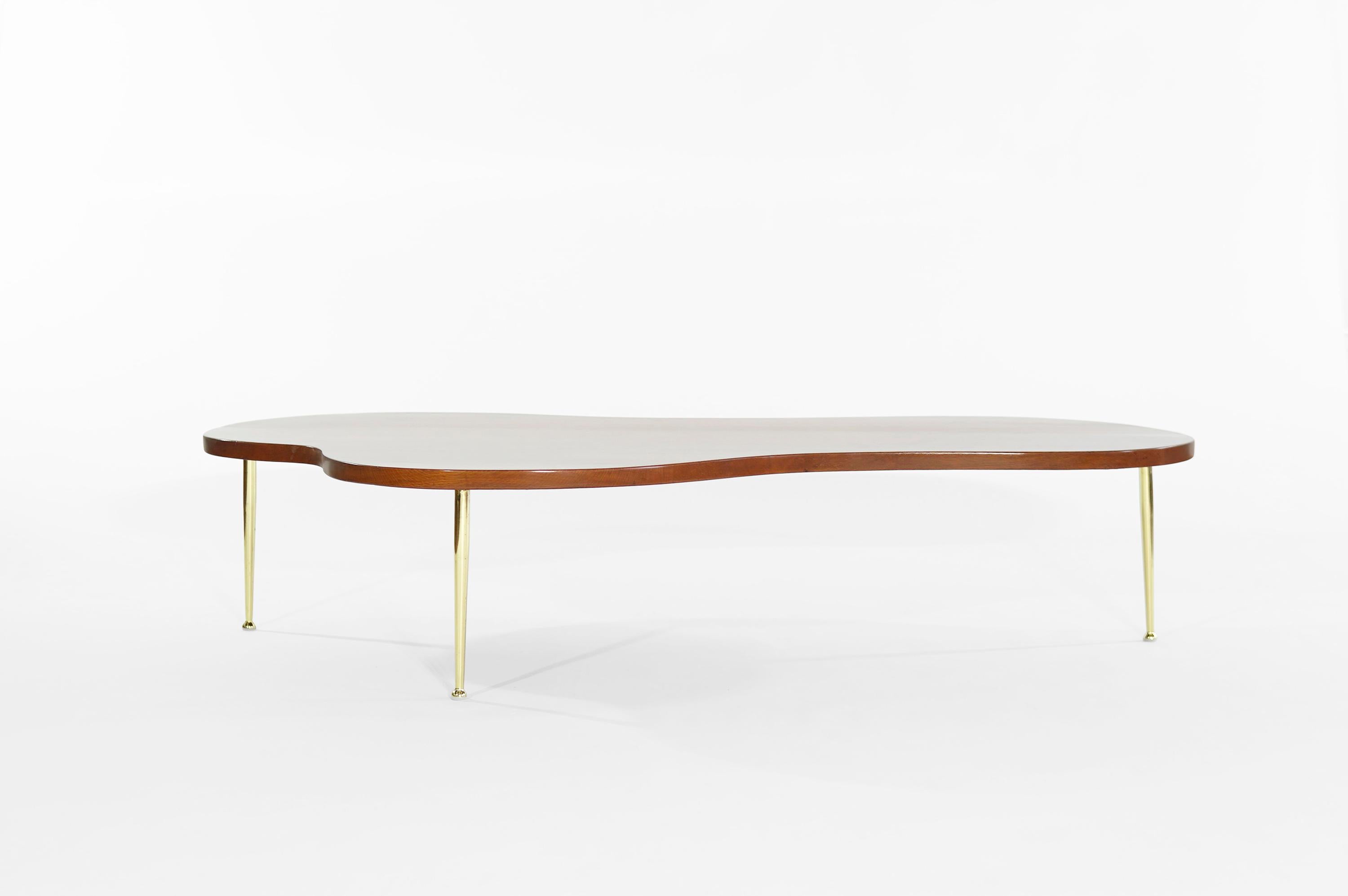 Iconic sculpted freeform coffee table designed by Robsjohn-Gibbings for Widdicomb. Fully restored oak top with hand polished tapered brass legs. Rare larger version.
      