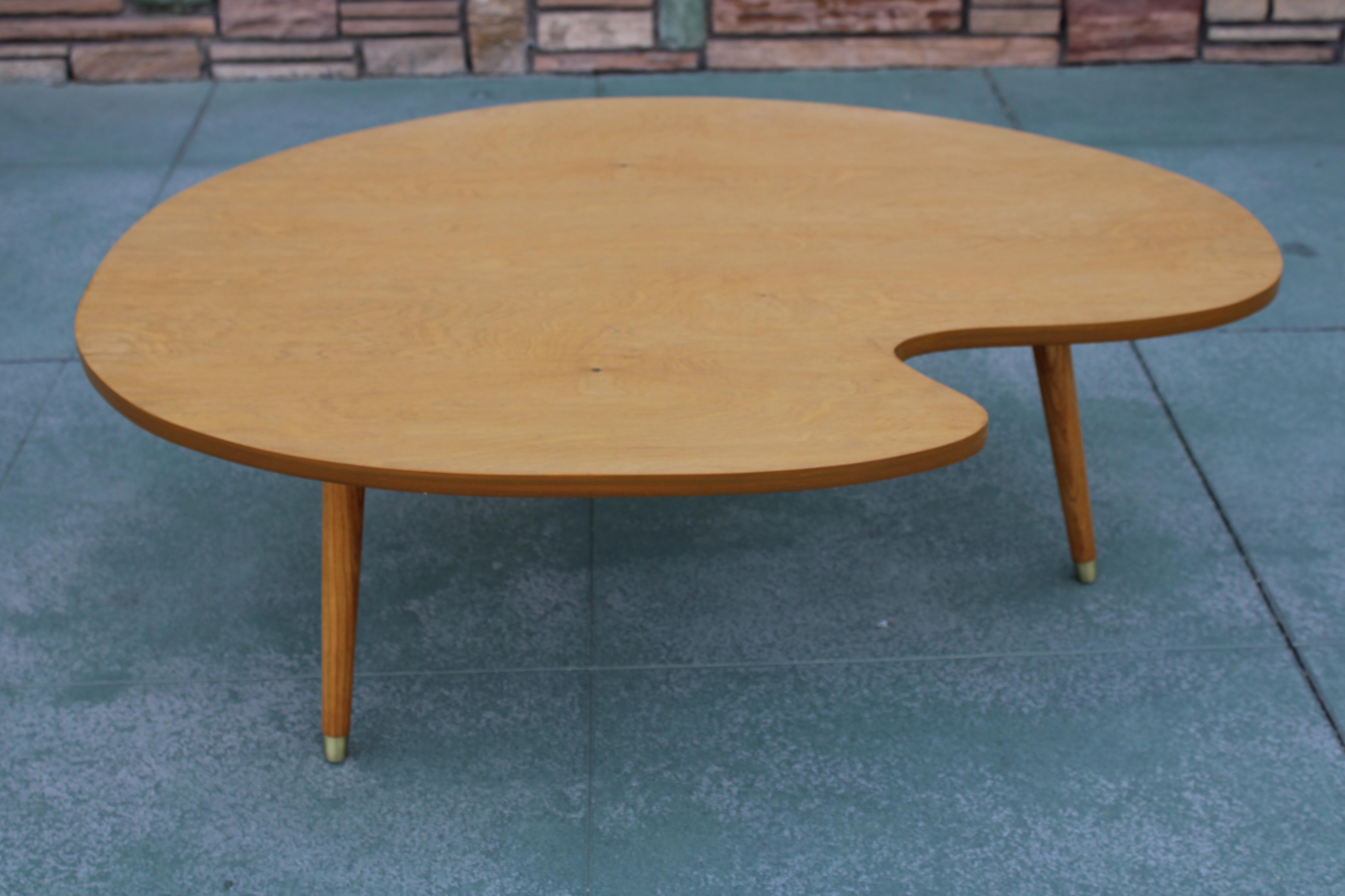 A late 40s to early 50s blonde wood coffee table with an artist's palette shaped top and tapered wood legs. Table measures 48