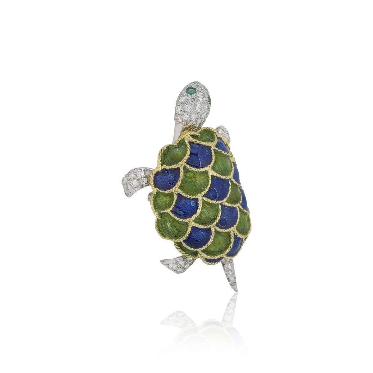 An 18k white and yellow gold articulated Turtle brooch. The Turtle is pave set with round brilliant cut diamonds with 2 emeralds for the eyes and has a blue and green patterned enamel shell. The head and tail of the turtle move freely. The diamonds