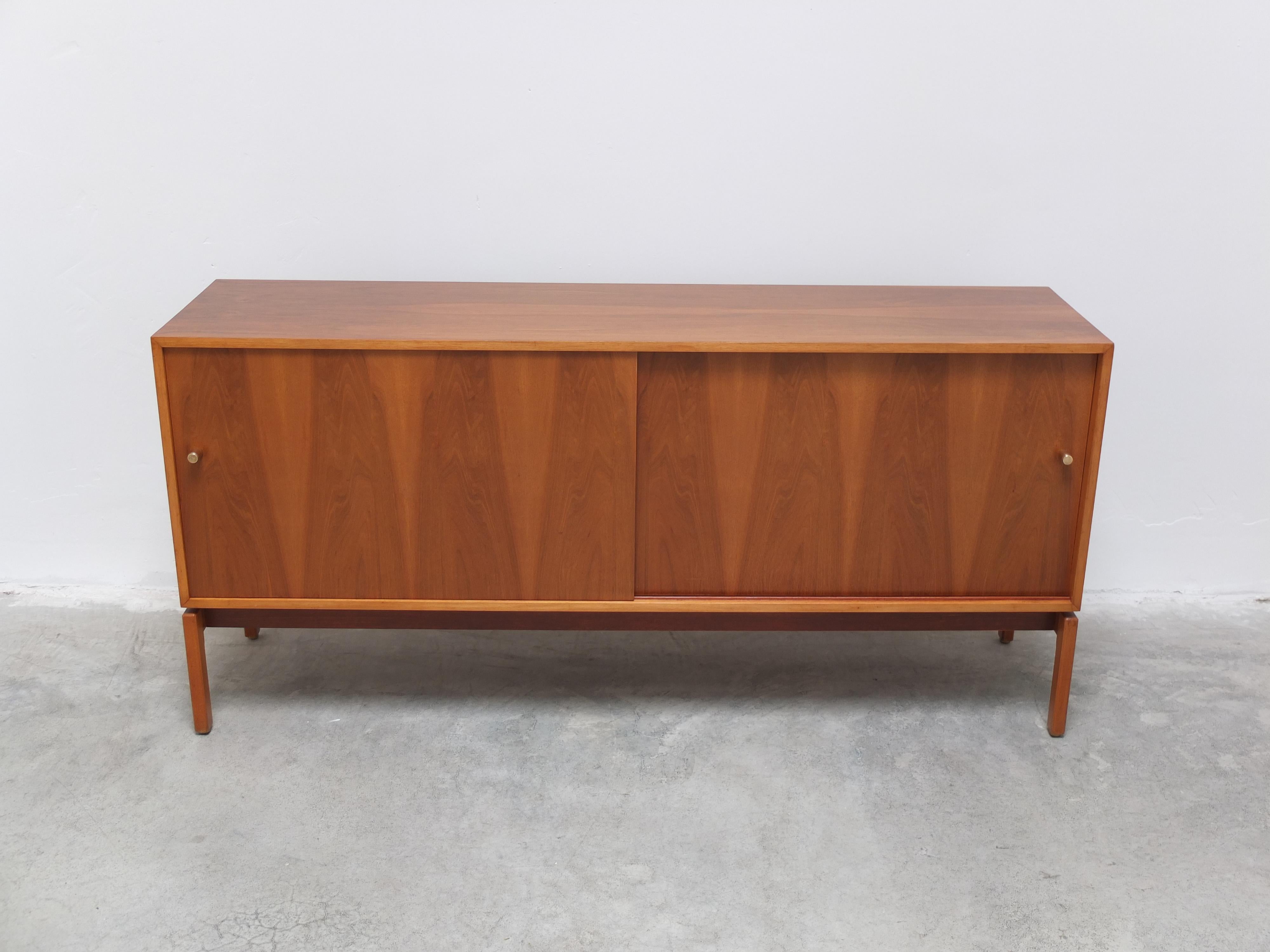 Rare compact sideboard with sliding doors from the ‘Abstracta’ series designed by Jos De Mey for Van Den Berghe-Pauvers during the 1960s. Highly decorative thanks to the beautiful walnut wood grain combined with the signature brass pulls. Remarkable