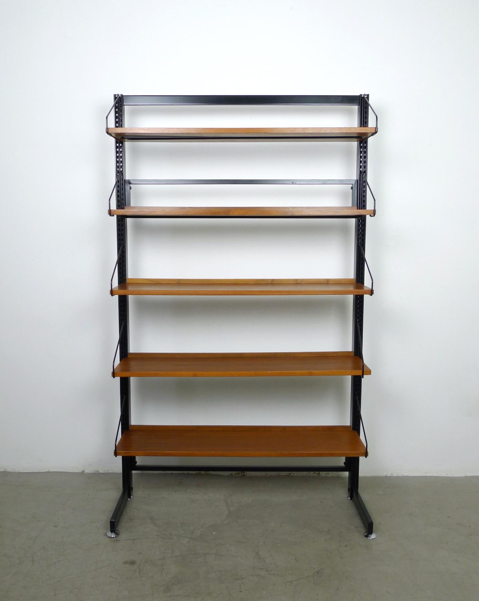 Freestanding floor bookcase with five shelves made of walnut, which can be arranged in height as desired. The black-lacquered uprights are made of metal and have two silver screw feet on the right and left, which can compensate for minor unevenness
