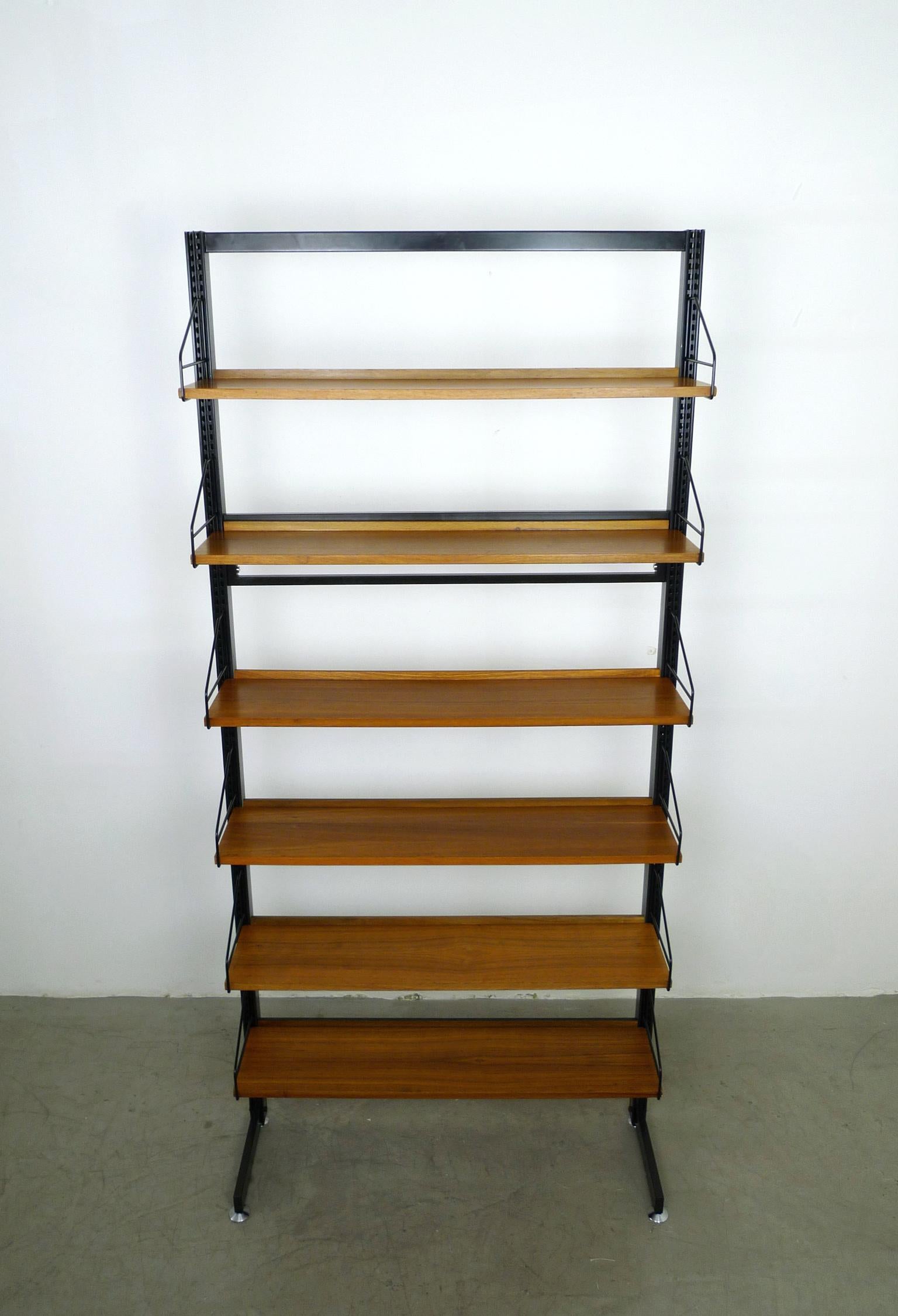 Freestanding floor bookcase with six shelves made of walnut, which can be arranged in height as desired. The black-lacquered uprights are made of metal and have two silver screw feet on the right and left, which can compensate for minor unevenness