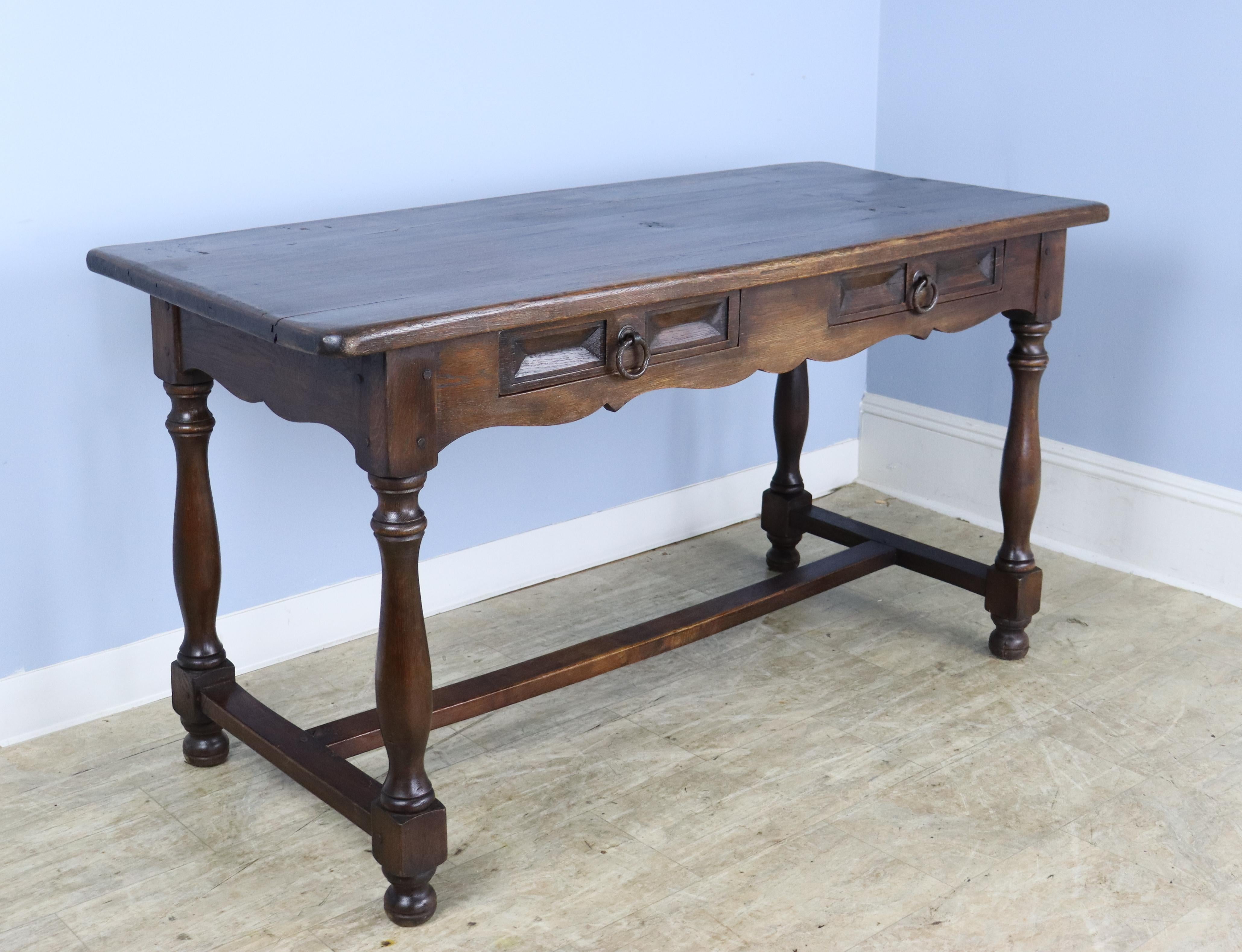 A handsome dark oak and chestnut Spanish desk with a trestle base and fancifully carved apron. Well finished, paneled back and 24 inch apron. A beautiful and stylish work surface.