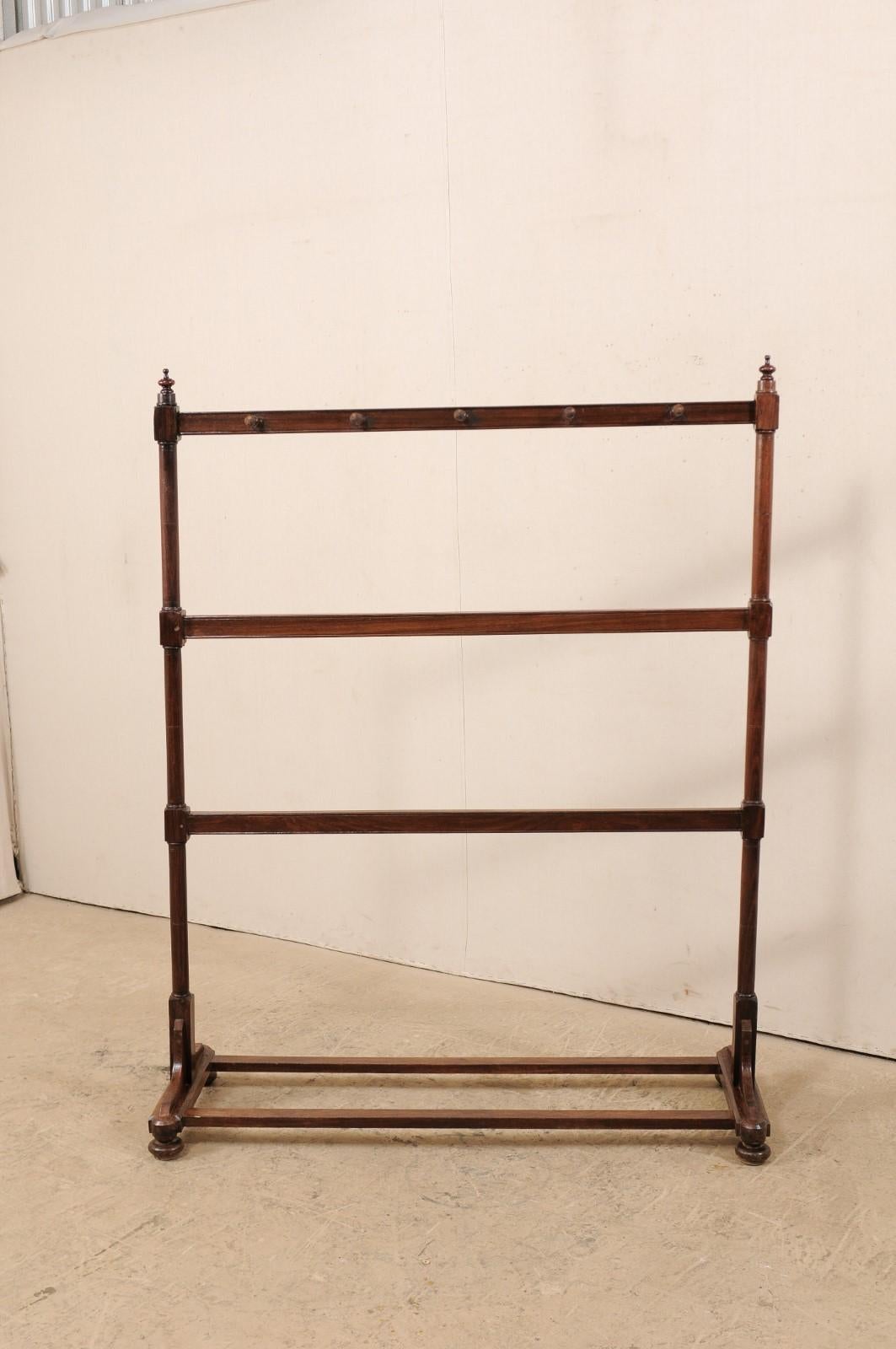 A vintage freestanding wooden rack. This coat hanging rack features five pegs place in horizontal fashion along the top, perfect for scarves and hats, atop two center rack/support posts beneath. The racks are flanked with round, slender posts, each