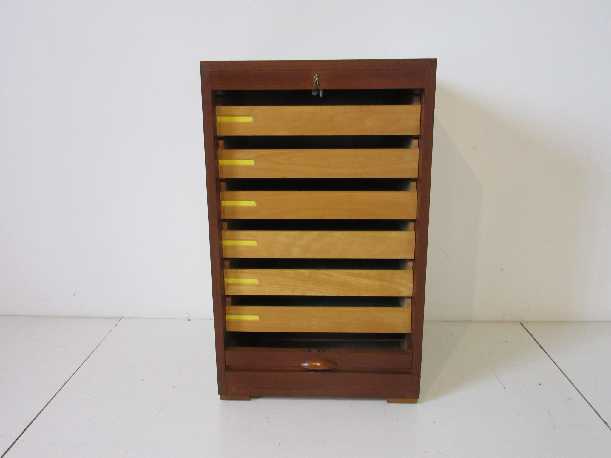 A Danish teak wood jewelry - watch chest / cabinet with roll down locking tabour door , brass key and six slide out drawers. Each drawer is felt lined to protect your Fine items and each drawer has a cutout for labels with yellow or orange for