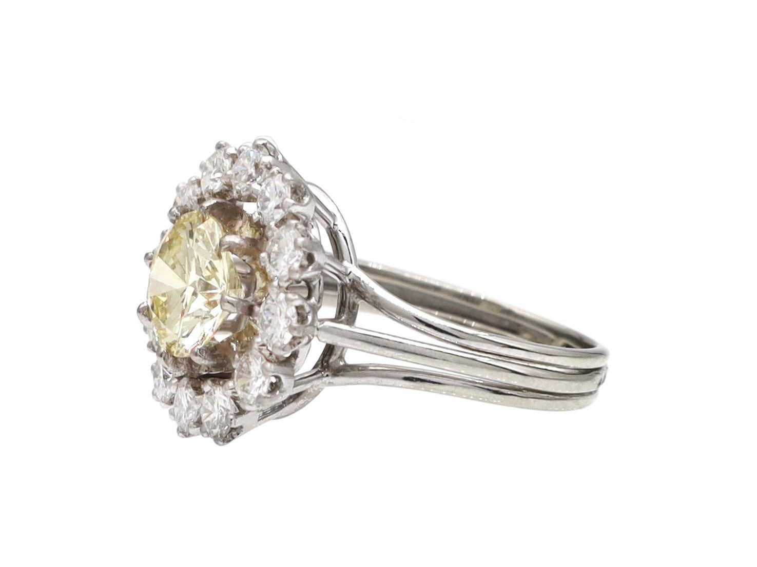 Vintage pale yellow diamond and diamond cluster ring in platinum and 18kt white gold. Centrally set with an estimated 1.18ct round brilliant cut light yellow diamond in a slightly raised claw setting, encircled with a row of round brilliant cut
