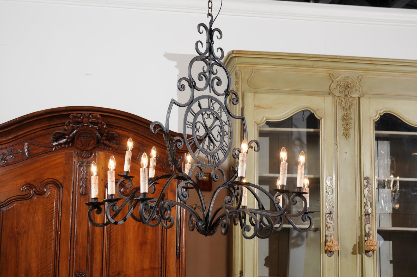 A French 12-light wrought iron chandelier from the 20th century with clock motif and scrolls. Created in France during the 20th century, this 12-light chandelier features a wrought iron armature showcasing various scrolls connected to one another,