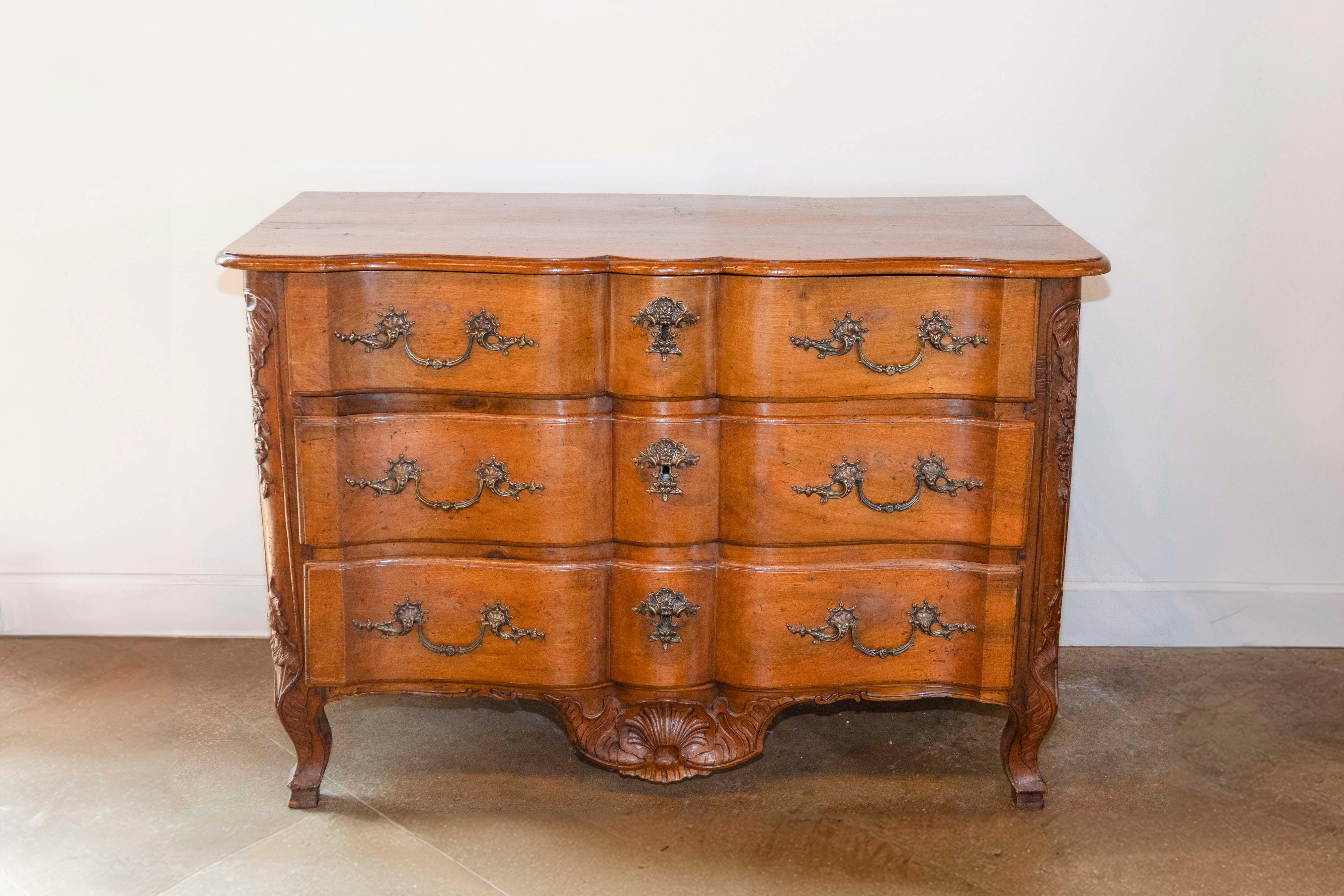 Commode en arbalete a tre cassetti in noce di epoca Regence realizzato alla maniera di Thomas e Pierre Hache, ébénistes di Grenoble. Questa commode Regence francese presenta un frontale a balestra, sormontato da un piano sagomato a due assi. I tre