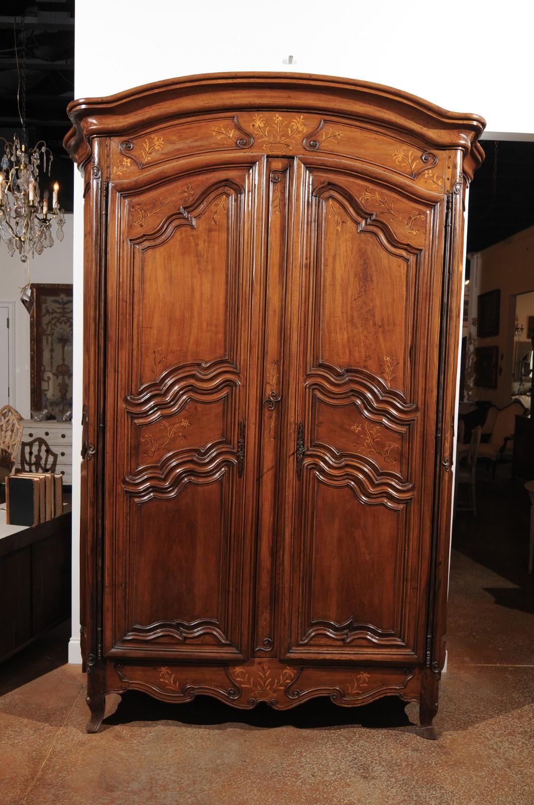 A French Louis XV period 18th century walnut armoire from the Rhône Valley, with floral inlay and curved sides. Born in France during the second quarter of the 18th century, this exquisite walnut armoire features a delicately arching molded cornice