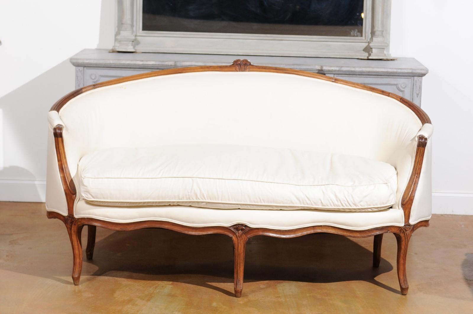 A French Louis XV period walnut settee from the mid-18th century, with cabriole legs and new upholstery. Born in France during the reign of King Louis XV 'Le Bien-Aimé' (the Beloved), this exquisite settee features a curved back flowing seamlessly