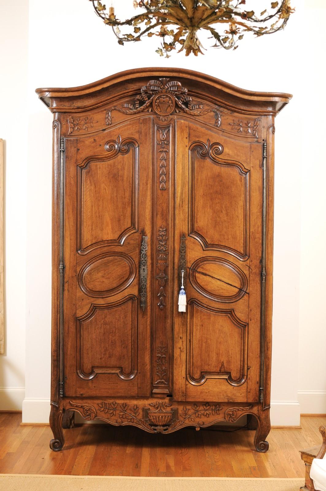 A French Louis XV period mid-18th century bonnet top walnut armoire from Nice, with ribbon-tied medallion and carved foliage. Handmade in Southern France during the reign of King Louis XV nicknamed the Bien-Aimé (the Beloved), this Niçoise walnut
