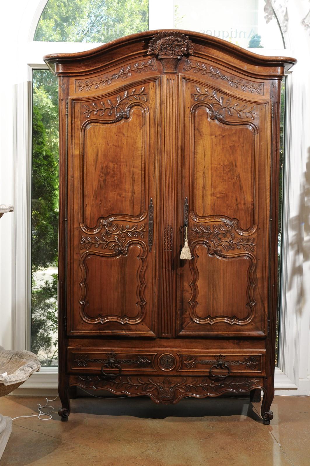 A French Louis XV period mid-18th century walnut armoire from Provence, with bonnet cornice, carved bouquet, molded door panels, foliage motifs and low drawer. Born in southern France during the reign of King Louis XV, this walnut Provençale armoire