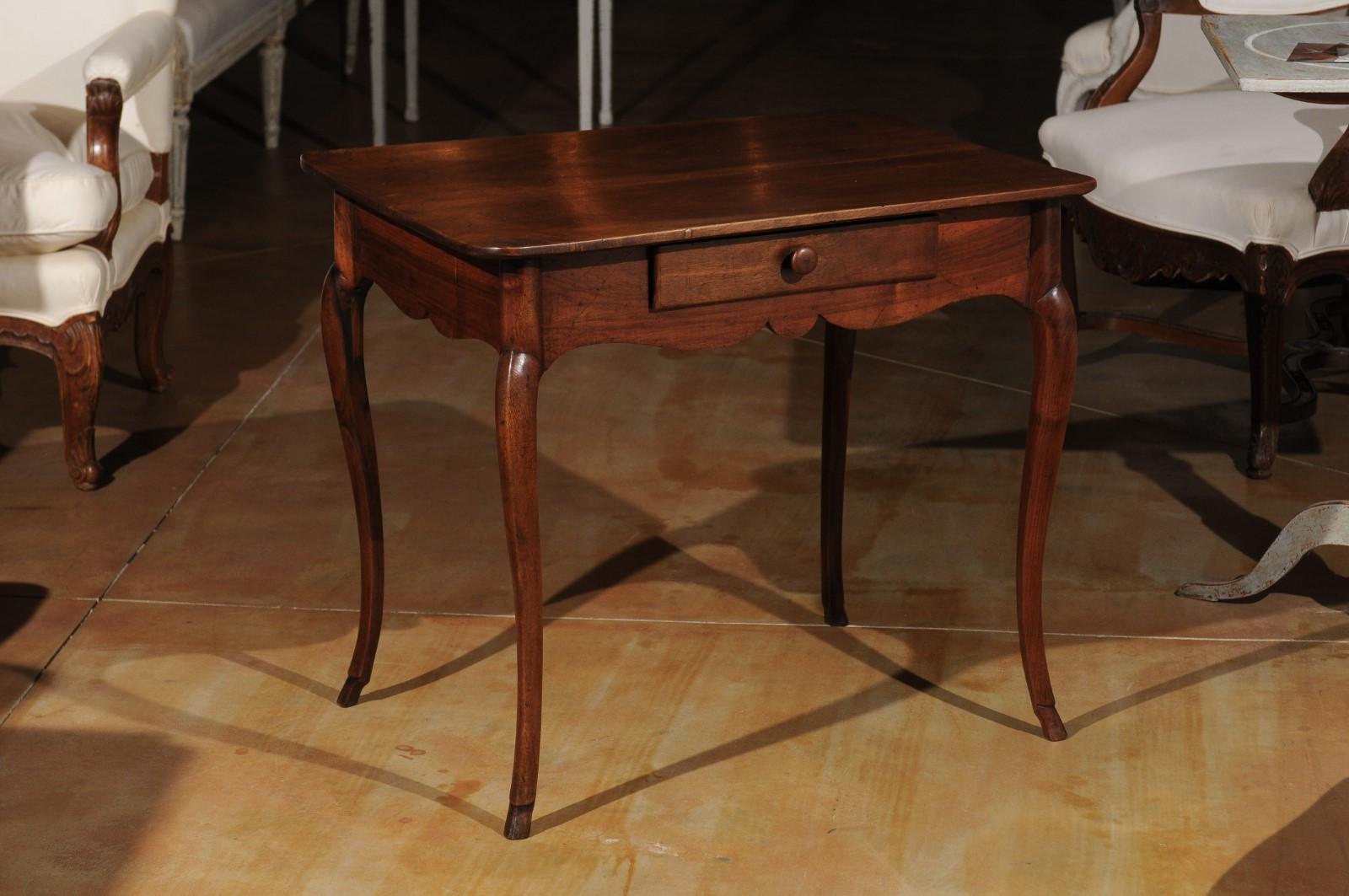 A French Louis XV period walnut table from the mid-18th century with acacia cabriole legs, scalloped apron and single drawer. Born in the Rhône Valley during the reign of King Louis XV 