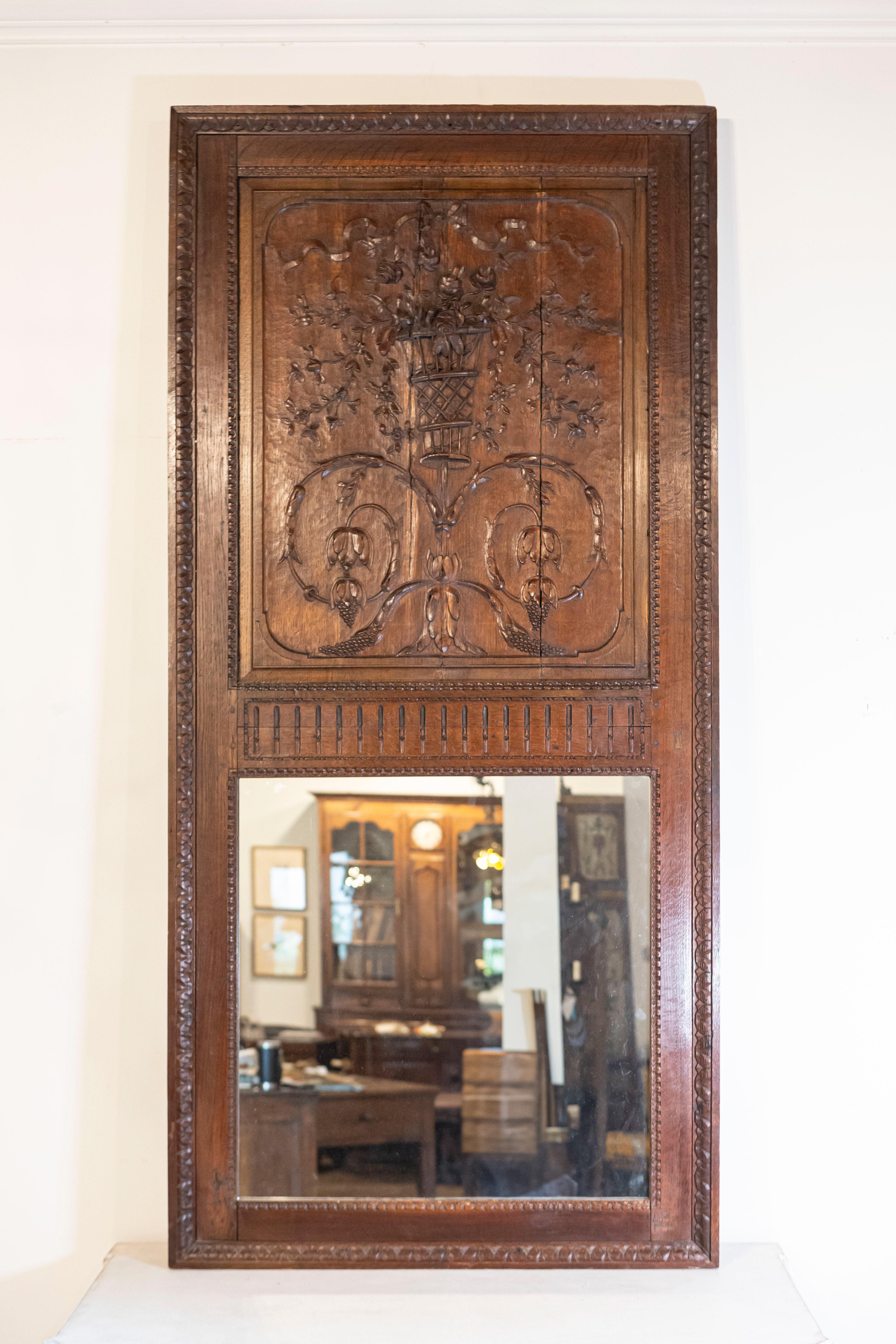 Specchio trumeau in quercia francese della metà del XVIII secolo con rinceaux intagliati e bouquet floreale. Creato in Francia nel 1750, questo specchio trumeau in quercia attira la nostra attenzione con i suoi due grandi rinceaux da cui pendono