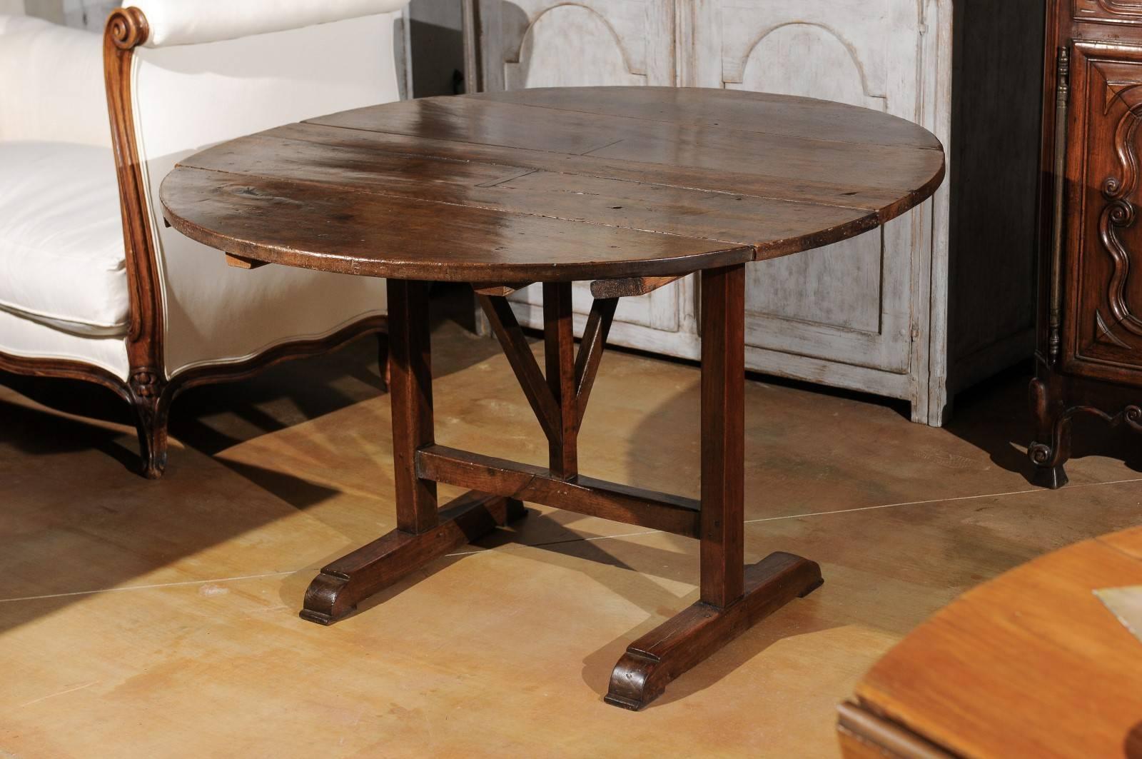 A French wine tasting table with circular top from the mid-18th century. This French wine tasting table features a round tilt-top, raised on a trestle base with rotating wedge, on which the top will rest once opened. Wine tasting tables were
