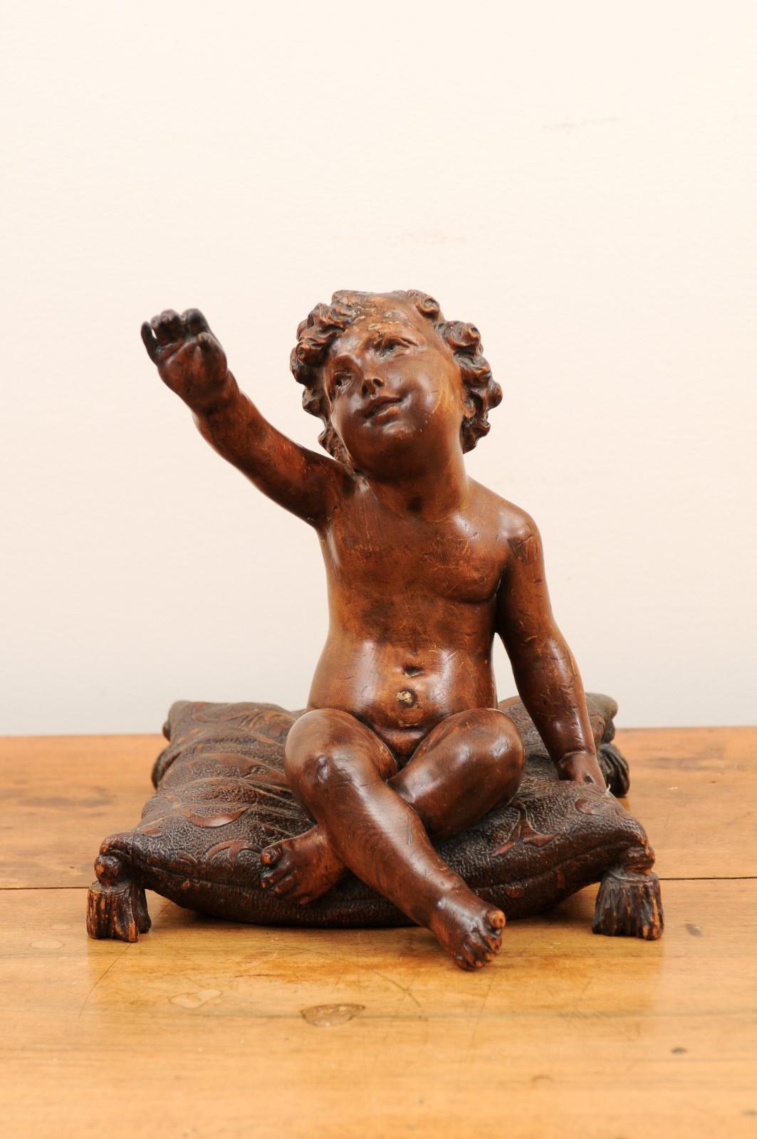 A French Baroque style walnut putto from the late 18th century, sitting on a pillow. Created in France during the last quarter of the 18th century, this walnut sculpture charms us with its skillful execution of a chubby putto sitting on a