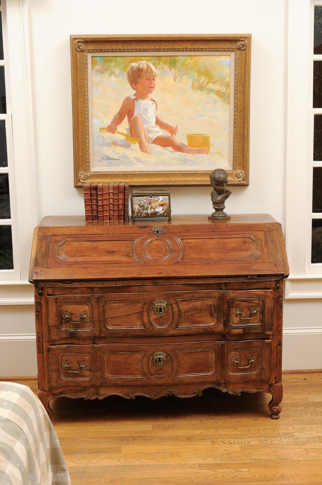 A French Transition period walnut slant front desk from the late 18th century, with drawers and carved apron. Created in France during the last decade of the 18th century, this desk showcases the stylistic characteristics of the Louis XV era, but