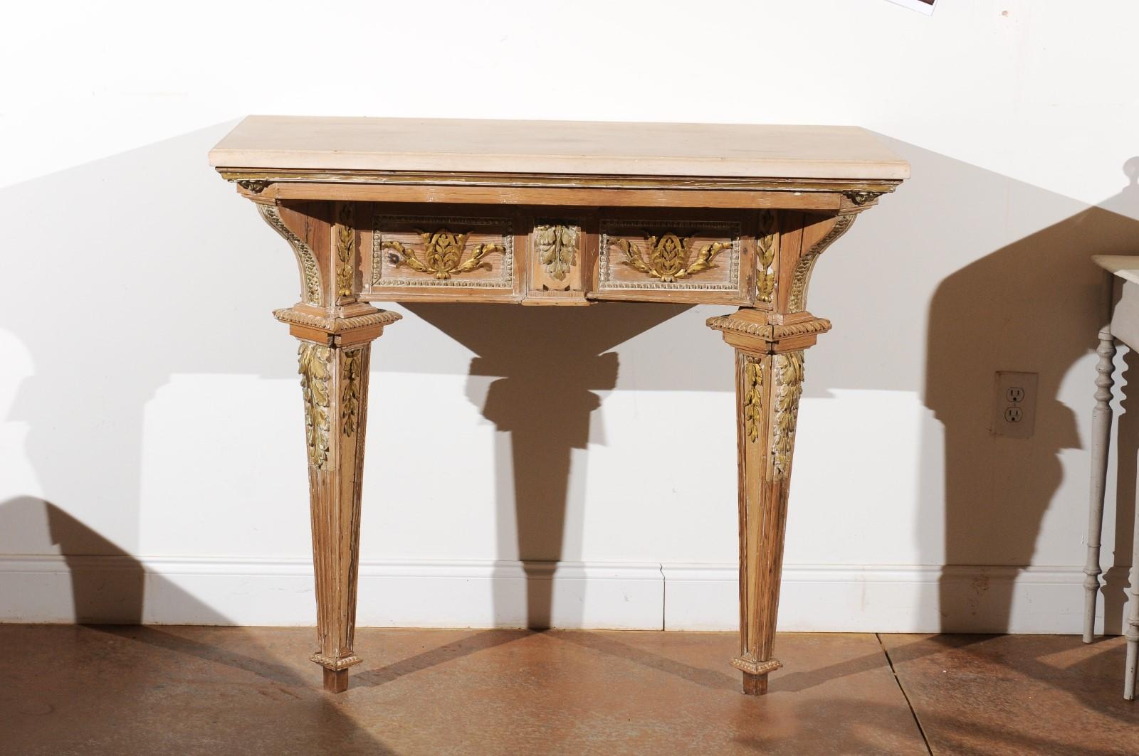 A French Louis XVI period hand carved and parcel-gilt wooden console table from the late 18th century, with new custom-made limestone top and tapered legs. Born in France during the reign of the last monarch of the Ancien Régime, this console table