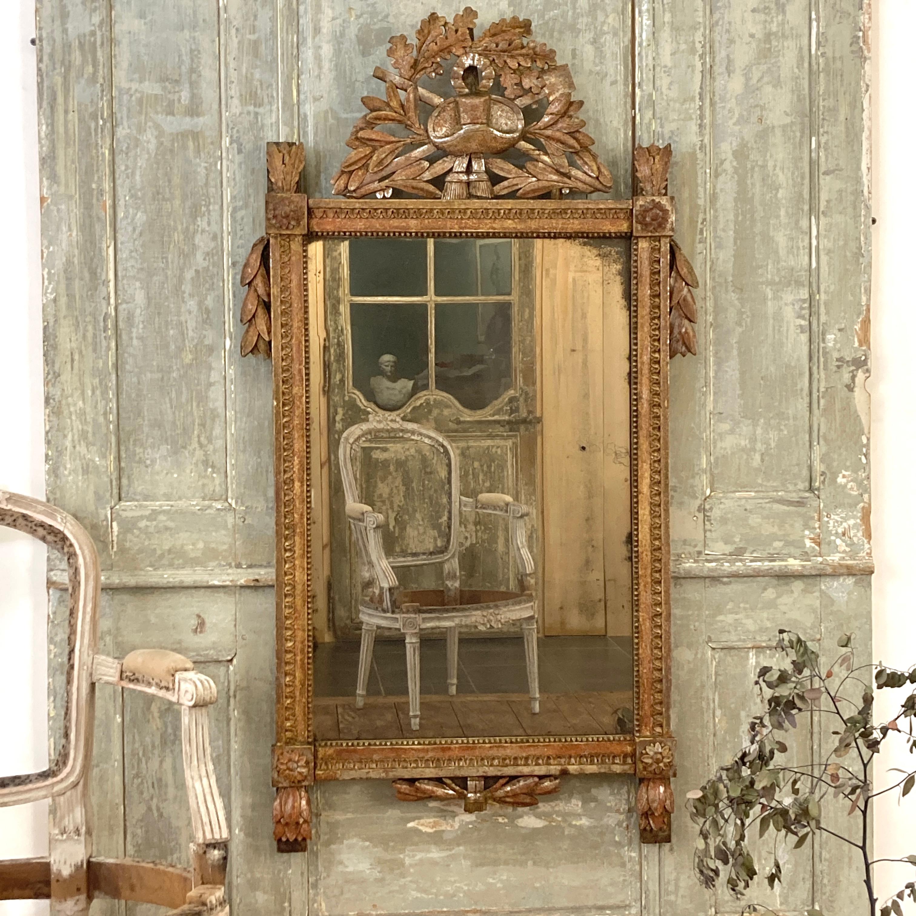 Miroir en bois doré d'époque Louis XVI, vers 1790, avec une crête sculptée représentant un thème de jardinage. Ce miroir en bois doré d'époque Louis XVI, datant d'environ 1790, est un splendide objet qui allie l'élégance du bois doré à un charme