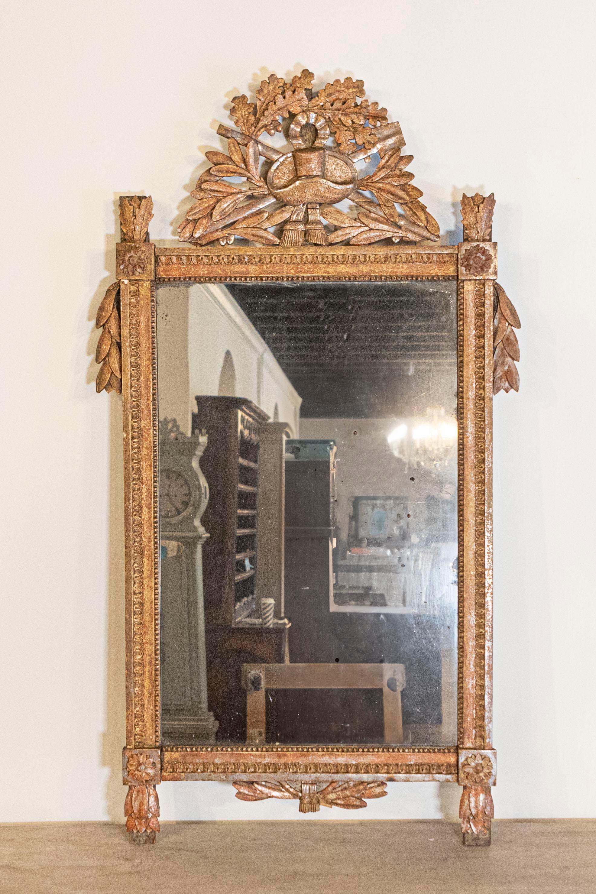 A French Louis XVI period giltwood mirror from circa 1790 with carved crest depicting a gardening theme. This French Louis XVI period giltwood mirror, dating back to circa 1790, is a splendid artifact that marries the elegance of giltwood with a