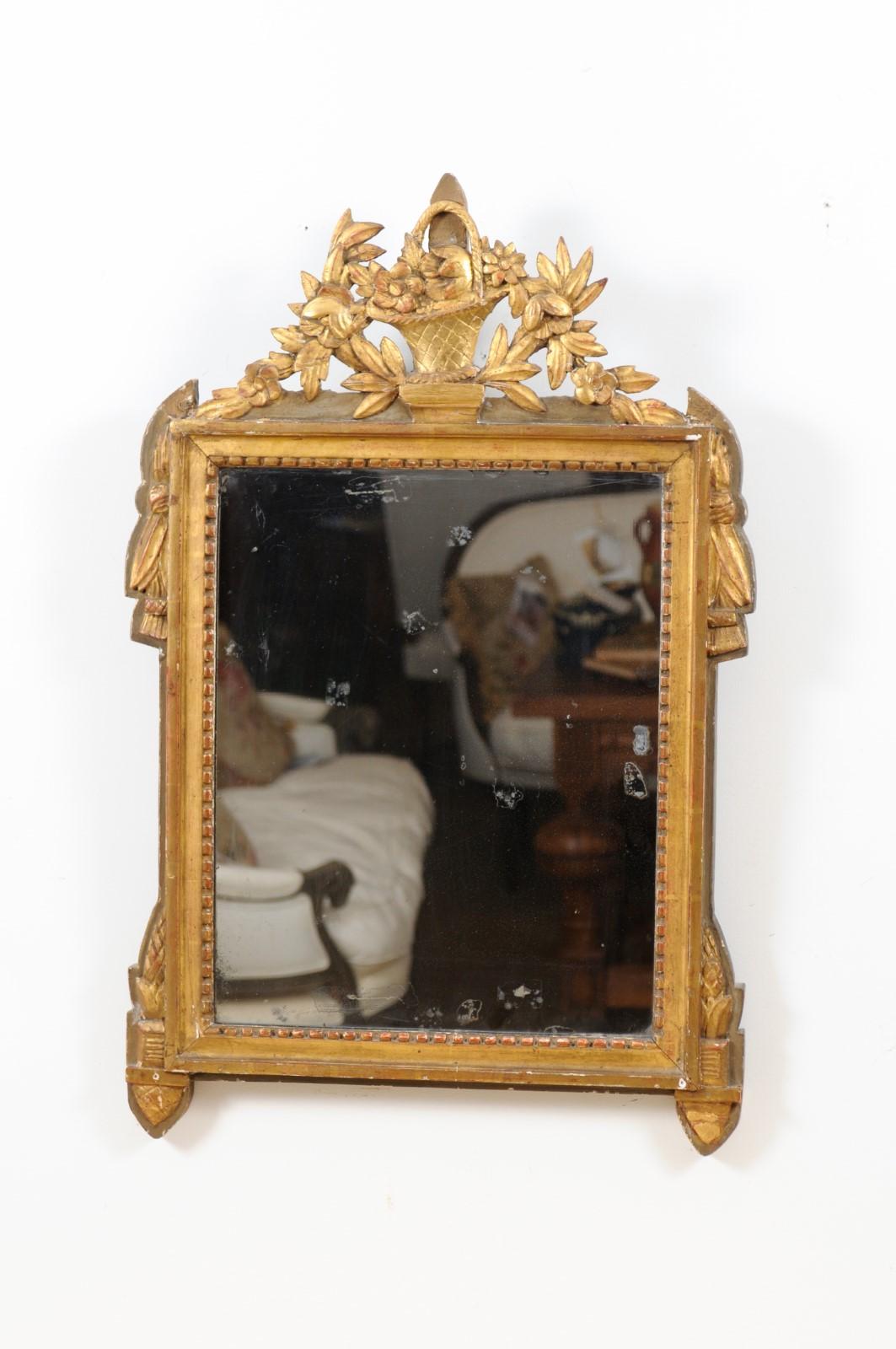 A French Louis XVI period carved giltwood mirror from the late 18th century, with wicker basket and floral garland. Created in France during the last decade of the 18th century, this giltwood wall mirror features a carved crest adorned with a wicker