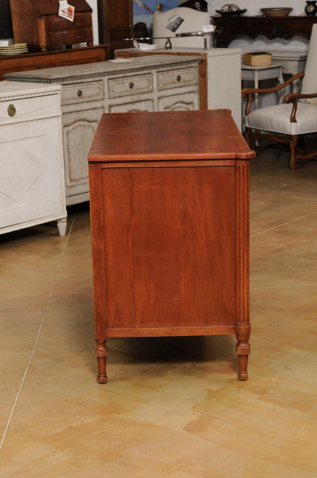 A French Louis XVI period cherry commode from the late 18th century, with three drawers and fluted side posts. Created in France during the last decade of the 18th century, this cherry commode features a rectangular top with rounded corners in the