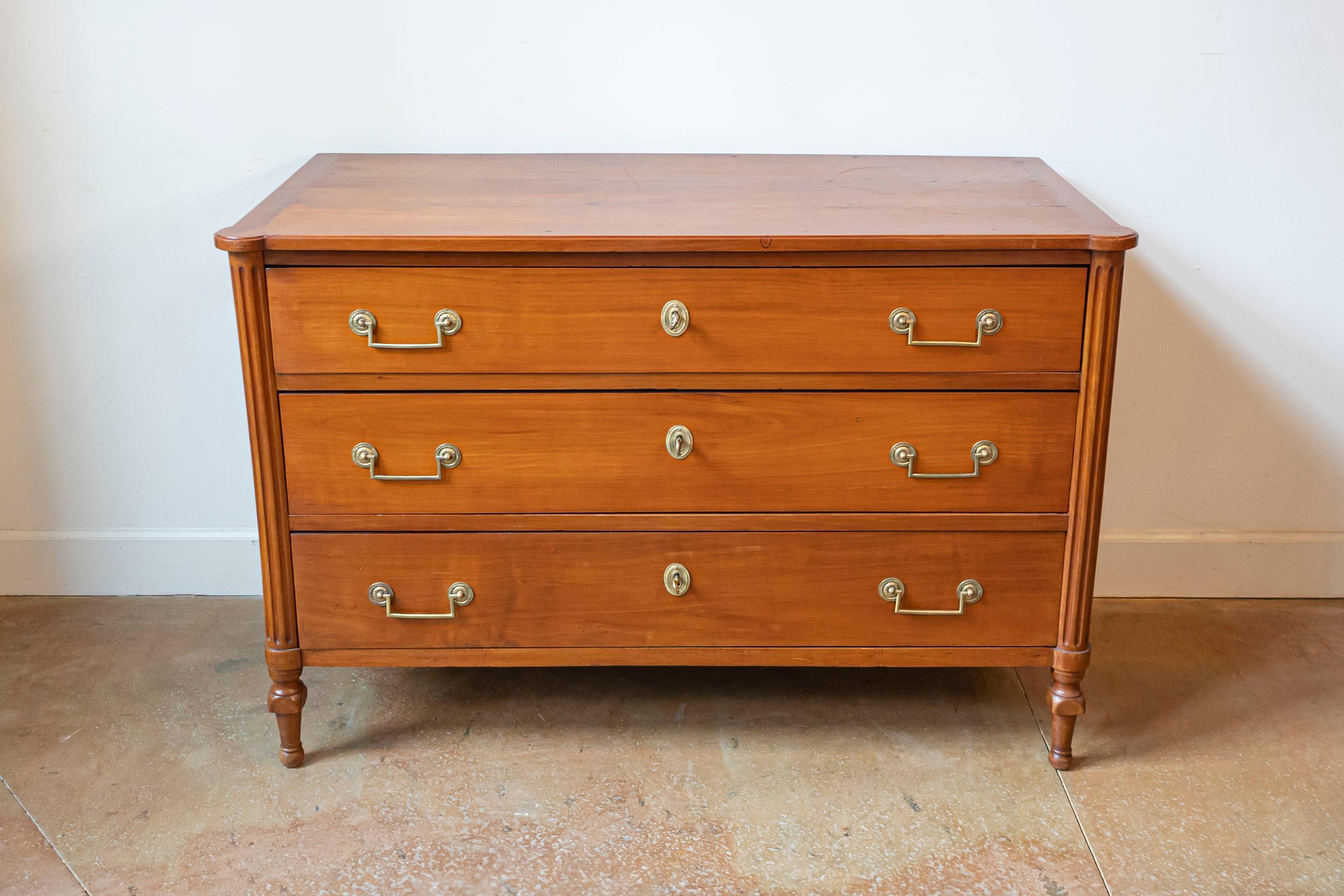 Commode en cerisier d'époque Louis XVI de la fin du XVIIIe siècle, à trois tiroirs et montants latéraux cannelés. Créée en France au cours de la dernière décennie du XVIIIe siècle, cette commode en merisier présente un plateau rectangulaire aux