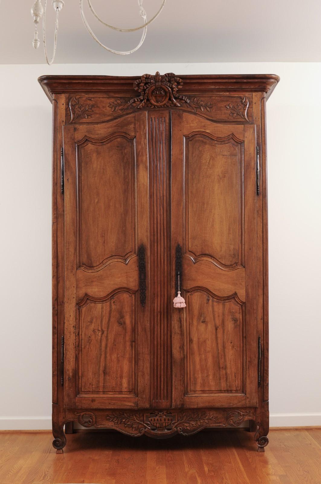 A French transition walnut armoire from the late 18th century, with carved crest and apron. Created in France during the last decade of the 18th century, this armoire showcases the delicate transition of style between the Louis XV and Louis XVI