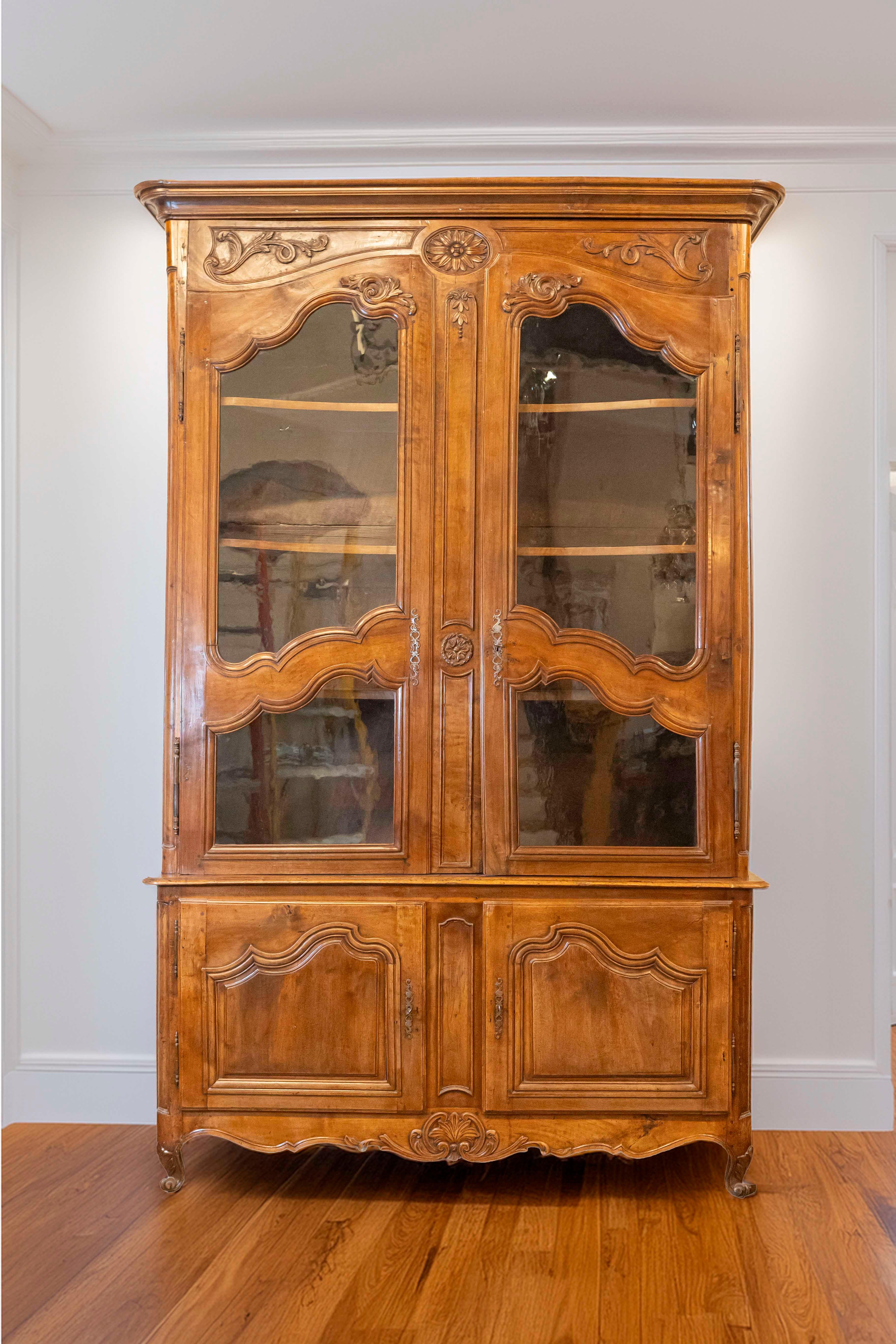 Buffet à deux corps en noyer de la fin du XVIIIe siècle, avec portes vitrées et motifs sculptés. Créé en France à la fin du règne de Louis XVI, ce buffet à deux corps en noyer présente une corniche moulurée surmontant deux portes ornées de motifs