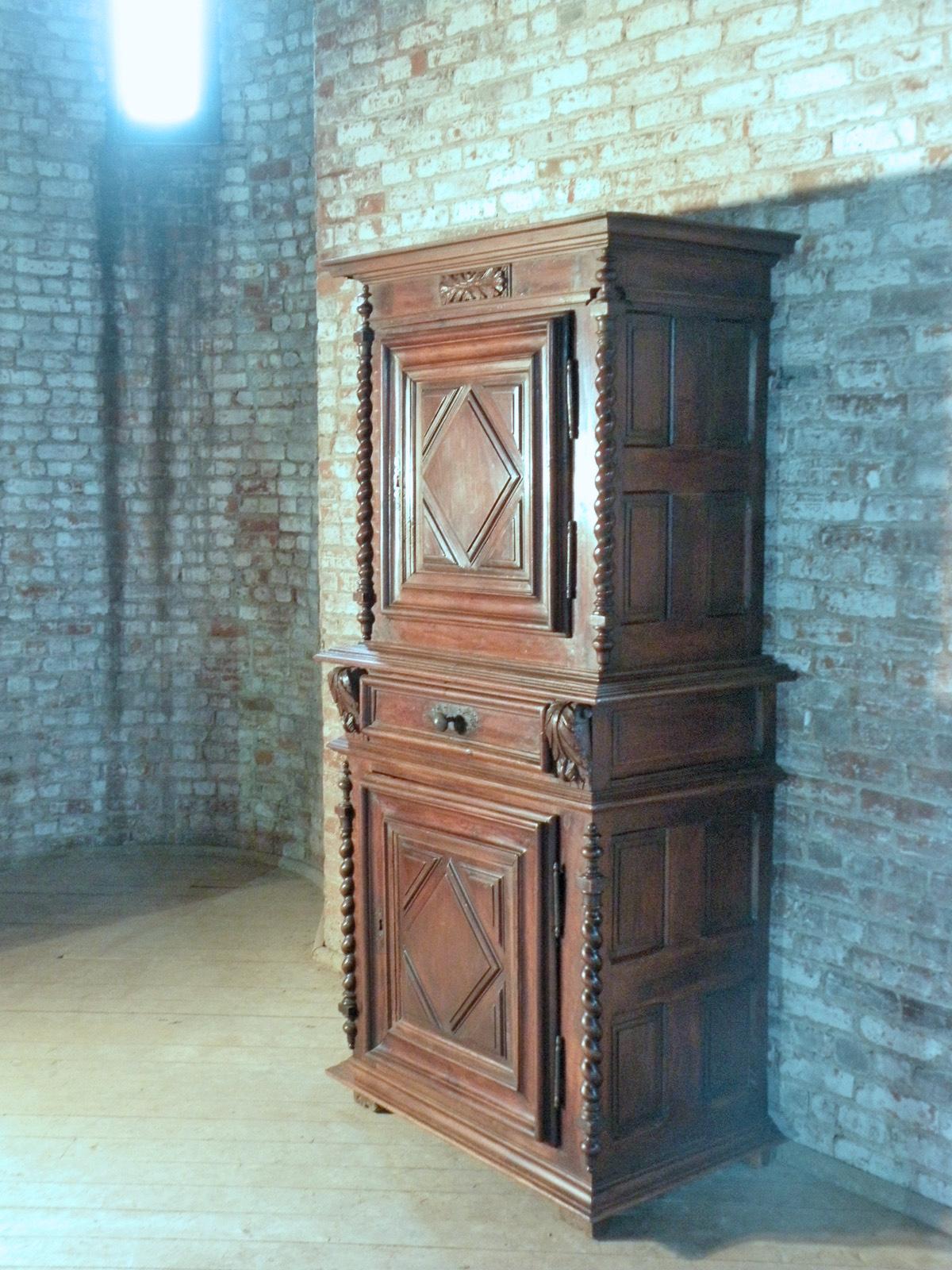 French Louis XIII Buffet a Deux-Corps / cabinet of unusual narrow size, in two parts, the upper part having one paneled door opening to an interior with one shelf, the sides paneled, the corners adorned with slender turned columns, the lower part