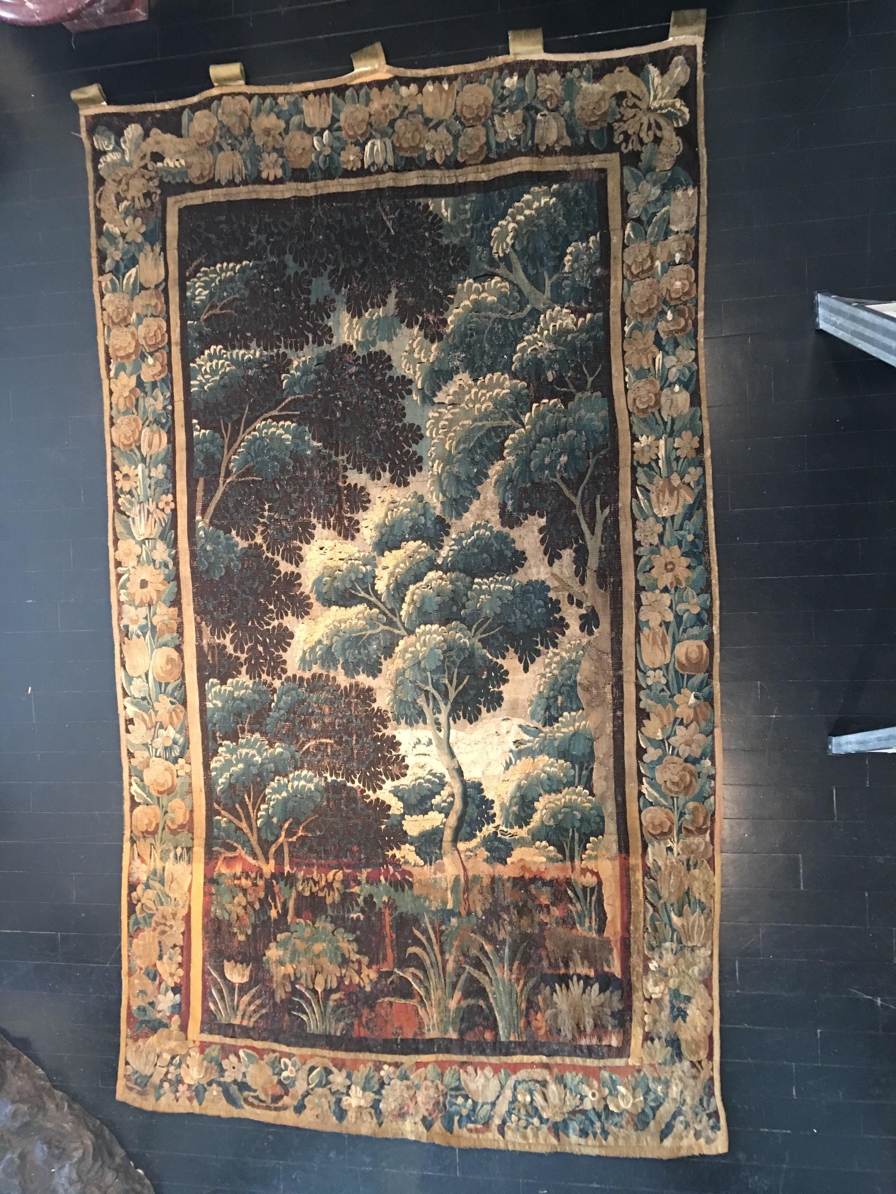 A large French Aubusson 17th century Verdure tapestry featuring a woodland setting enclosed within a scrolling foliate border. Linen, with wool and silk inlay. Handmade in vibrant hues in the classical palette of greens and indigos. Lush composition