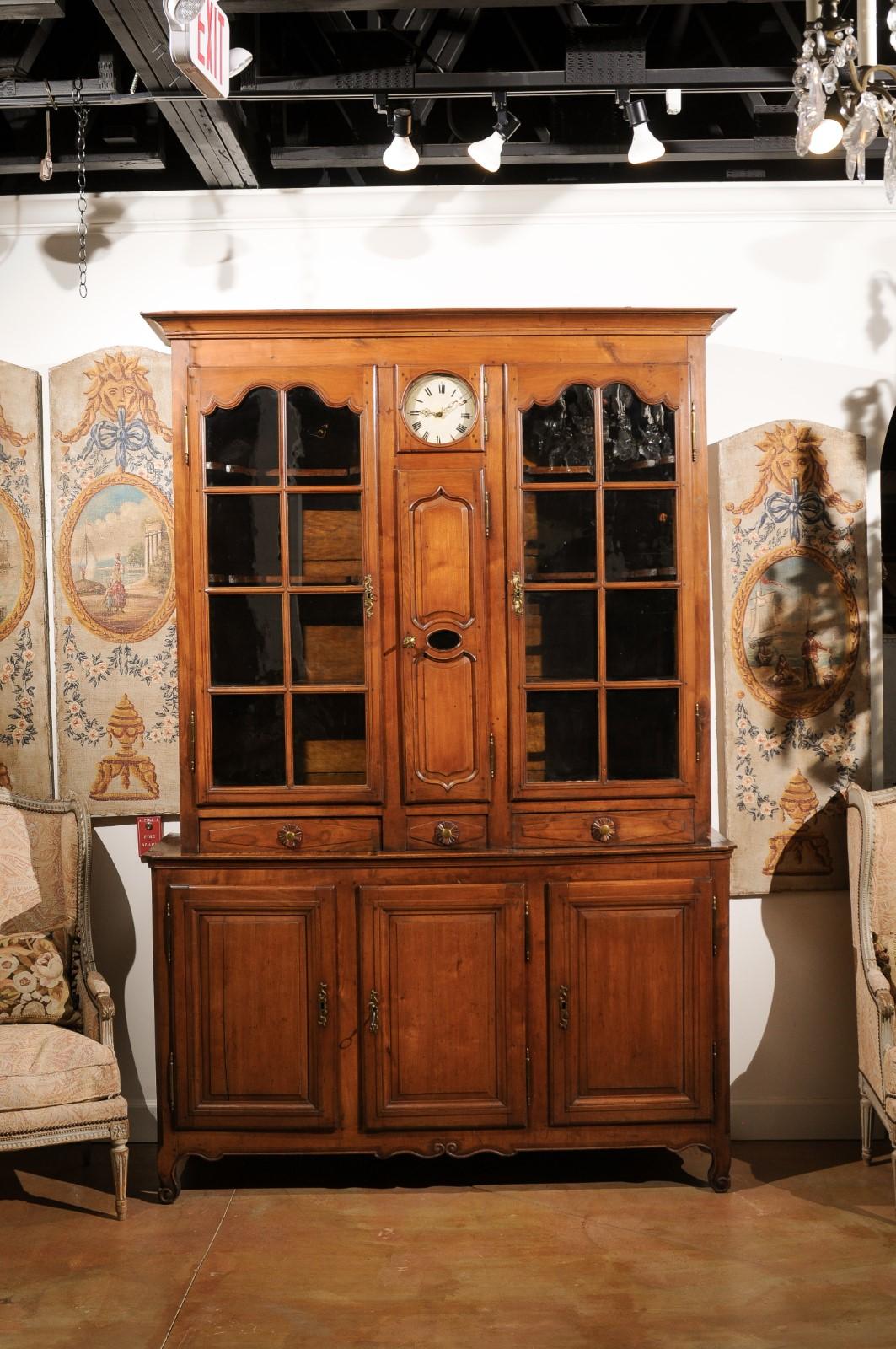 A French Louis XV style cherry buffet à deux-corps from the early 19th century, with glass doors and round clock. Created in France at the beginning of the reign of Emperor Napoléon I, this cherry buffet à deux-corps features a beveled cornice
