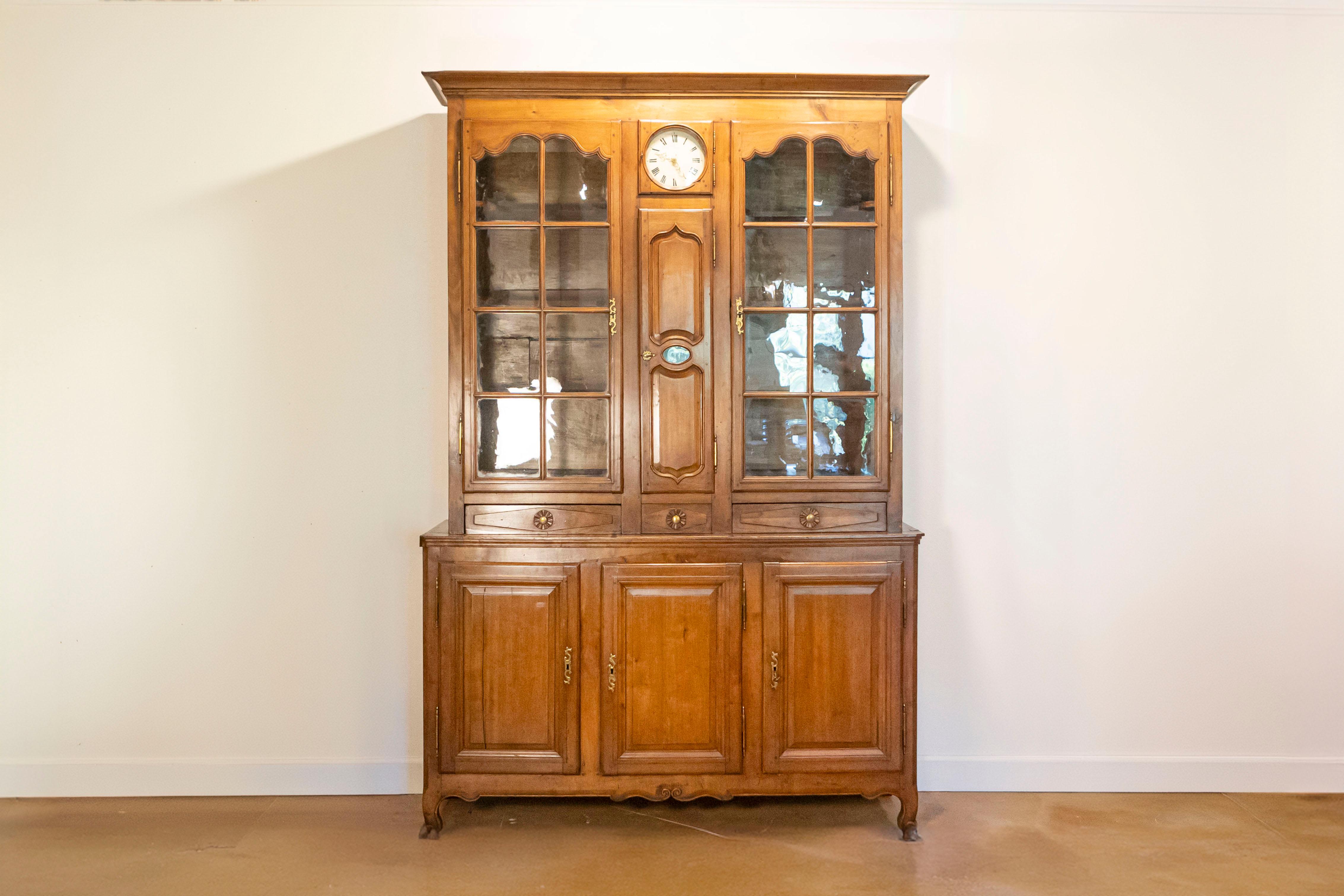 A French Louis XV style cherry buffet à deux-corps from the early 19th century, with glass doors and round clock. Created in France at the beginning of the reign of Emperor Napoléon I, this cherry buffet à deux-corps features a beveled cornice