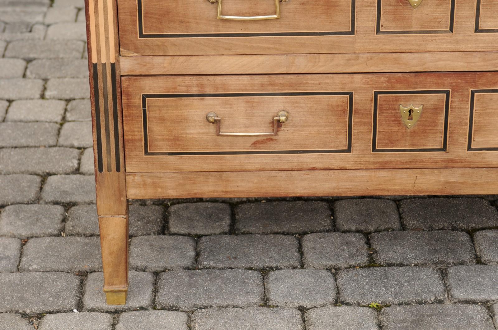 A French Directoire period three-drawer walnut commode from the early 19th century, with white marble top and ebonized accents. Born in the early years of the 19th century, this French walnut commode features a rectangular white veined marble top,