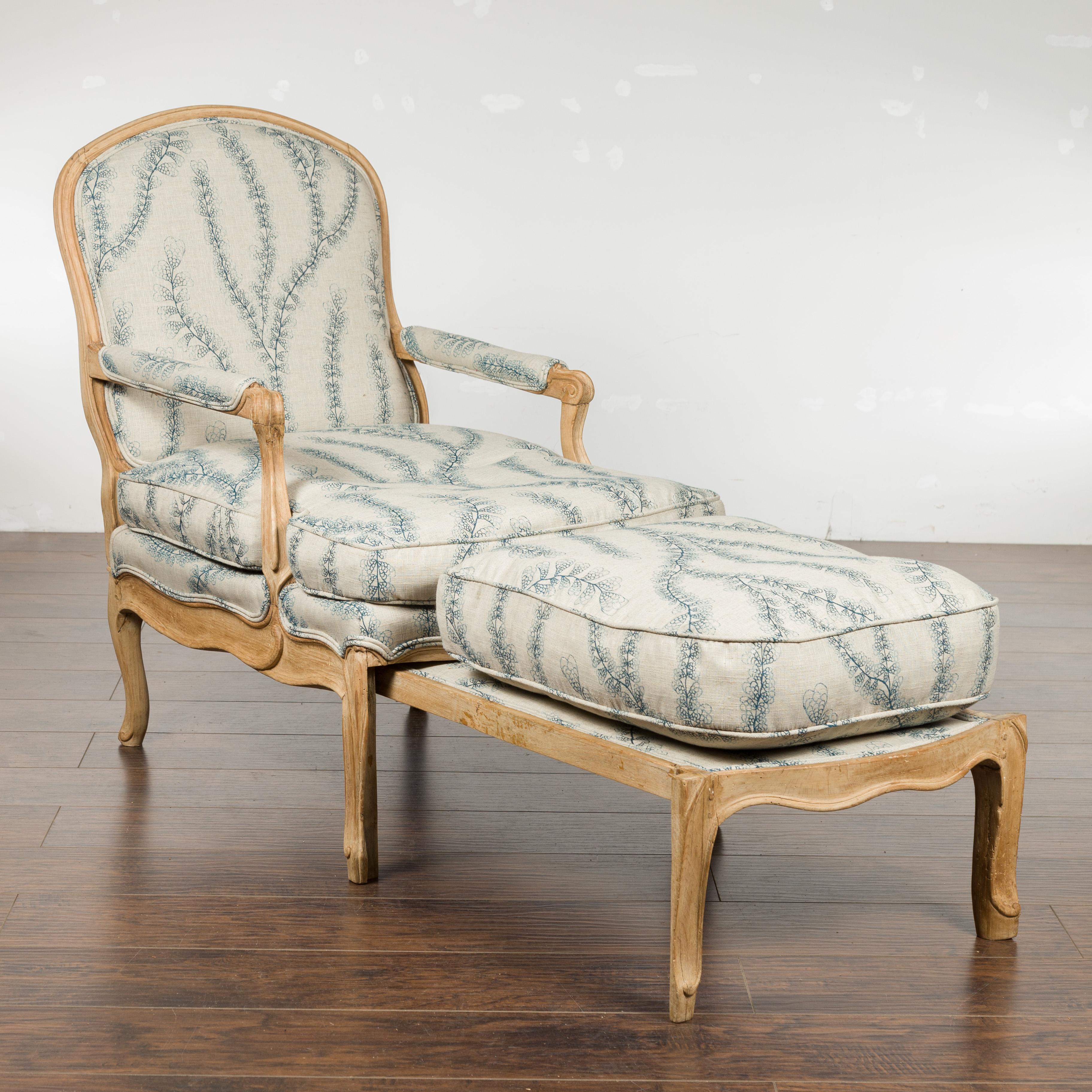 A French Louis XV style oak lounge chair from the early 19th century, with natural patina and foliage-adorned upholstery. Created in France during the early years of the 19th century, this oak fauteuil features a pull-out in the front transforming