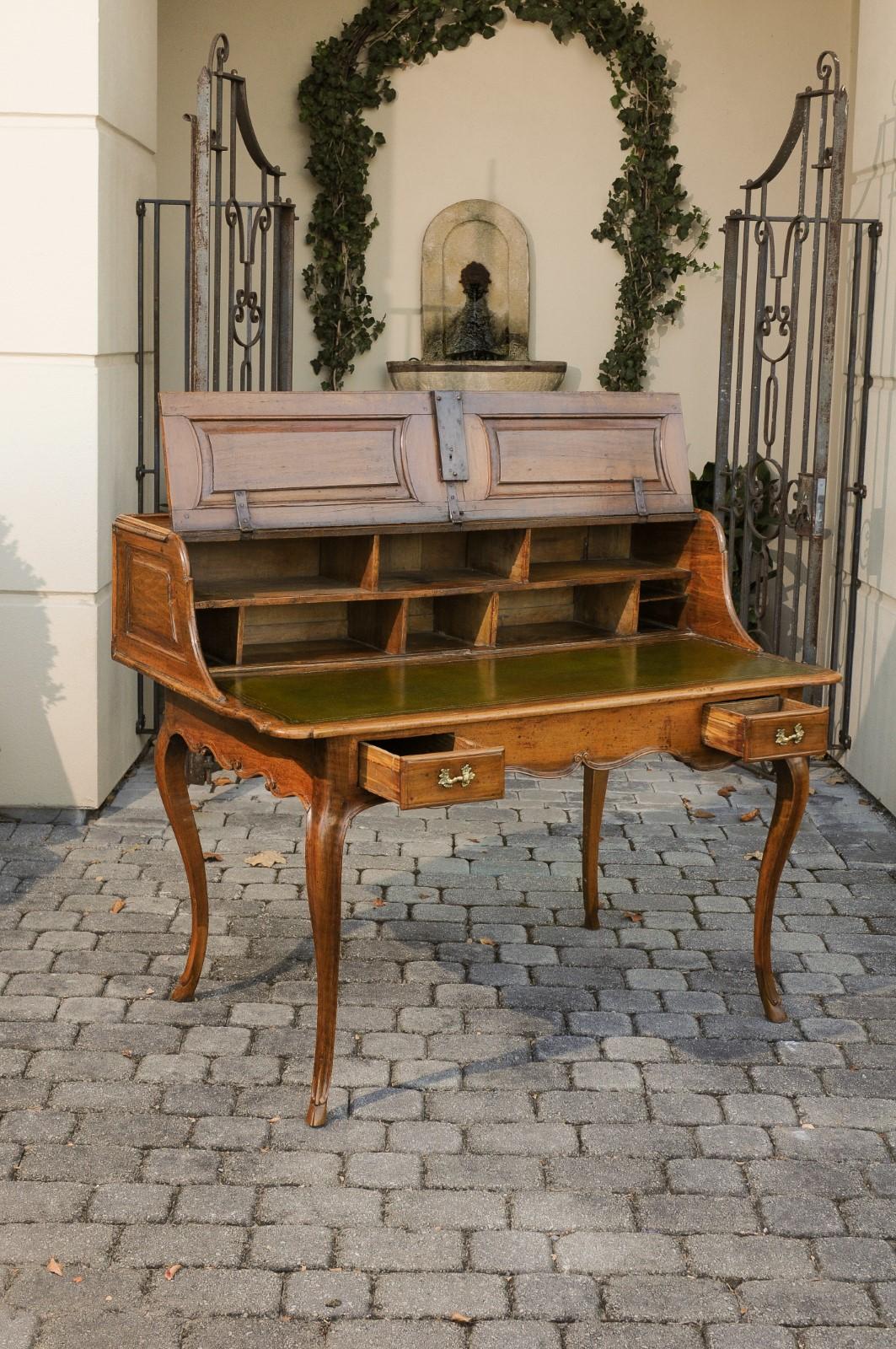 A French Louis XV style walnut desk from the early 19th century, with lifting panel, green leather writing surface and cabriole legs. Born in France during the early years of the 19th century, this exquisite desk features a writing area overhanging