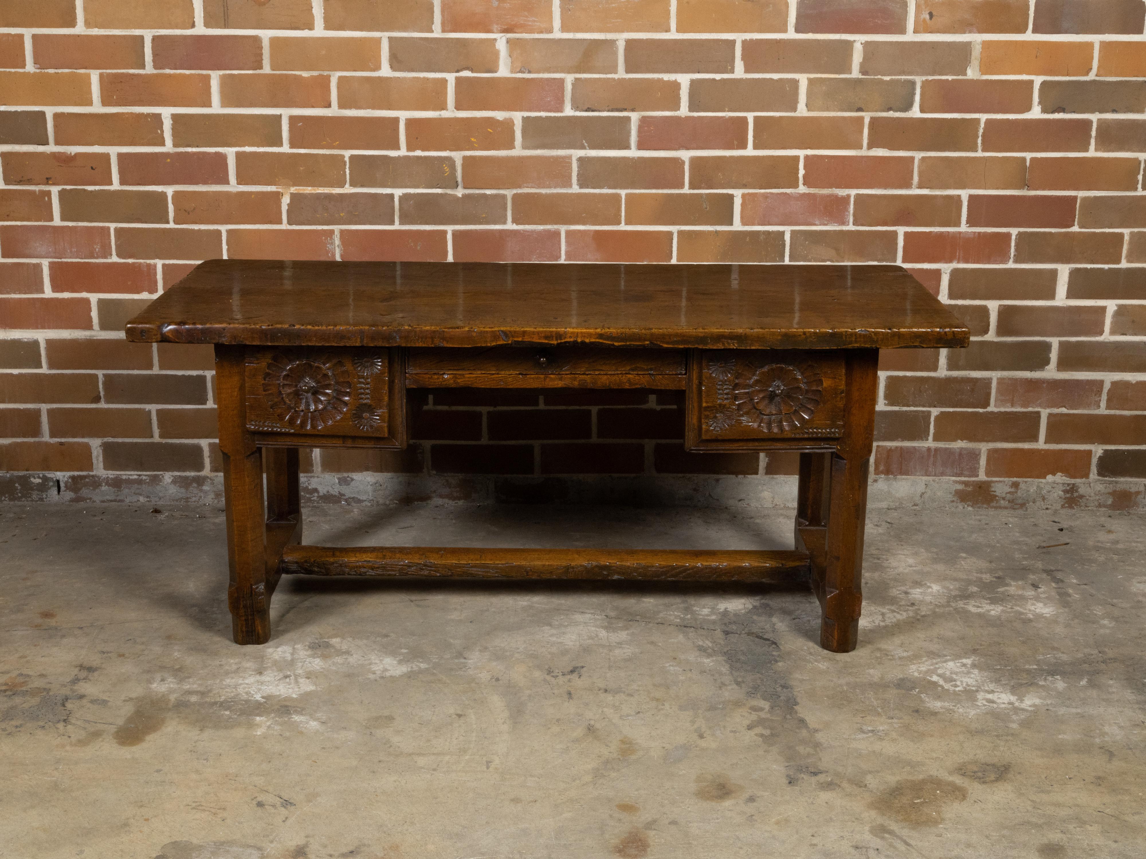 A French walnut desk from the early 19th century with three drawers, carved motifs, H-Form cross stretcher and nice patina. Created in France during the early years of the 19th century, this walnut desk features a rectangular top with nice aging and