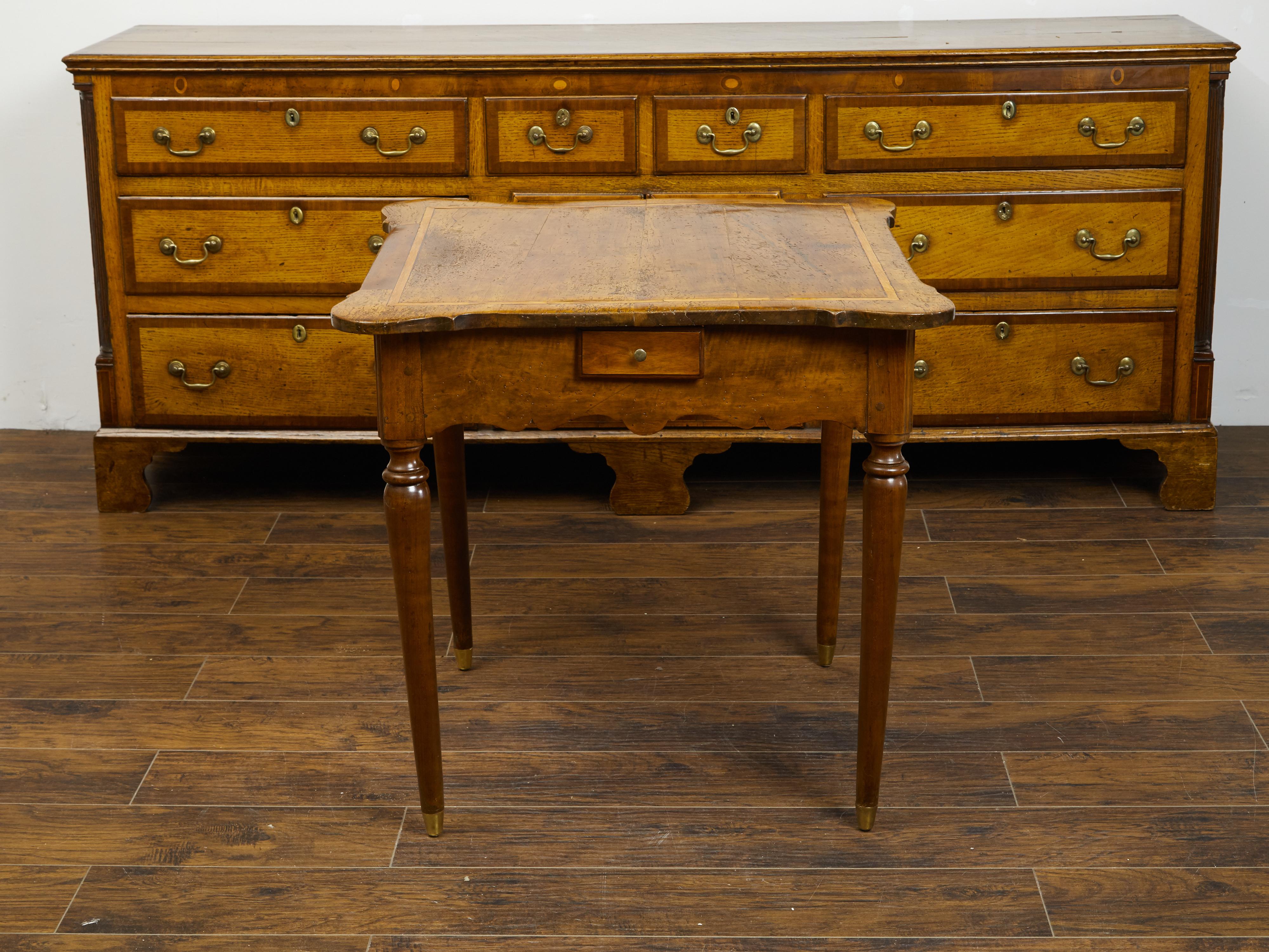 A French walnut table from the early 19th century, with banding, four small drawers and carved apron. Created in France during the early years of the 19th century, this walnut table features a shaped planked top with rounded corners and banding,