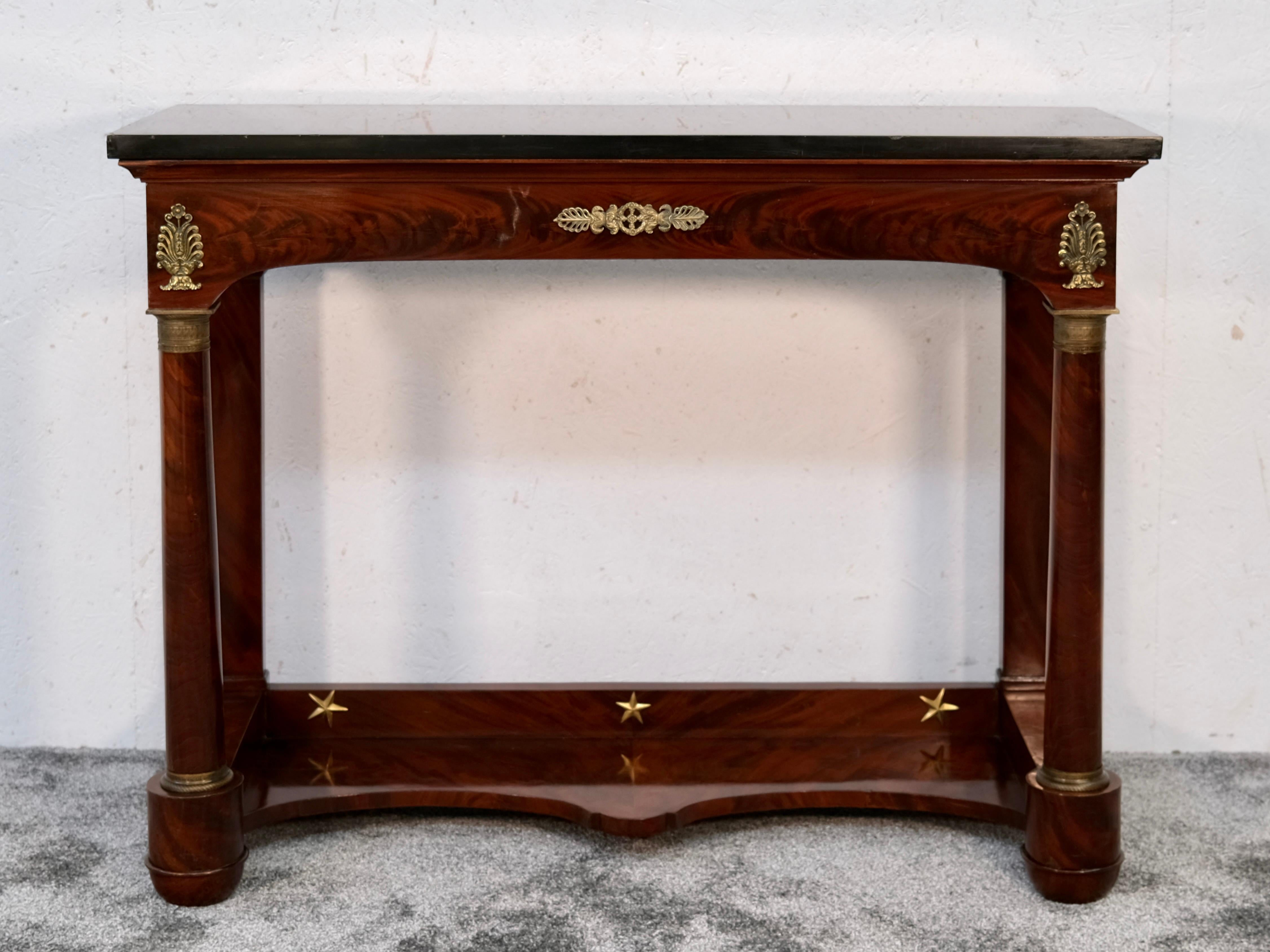 This refined French Empire console table, crafted circa 1810, showcases the sculptural clarity and symmetry typical of early 19th-century design. Built from beautifully grained mahogany, the piece features finely detailed bronze appliqués and stands