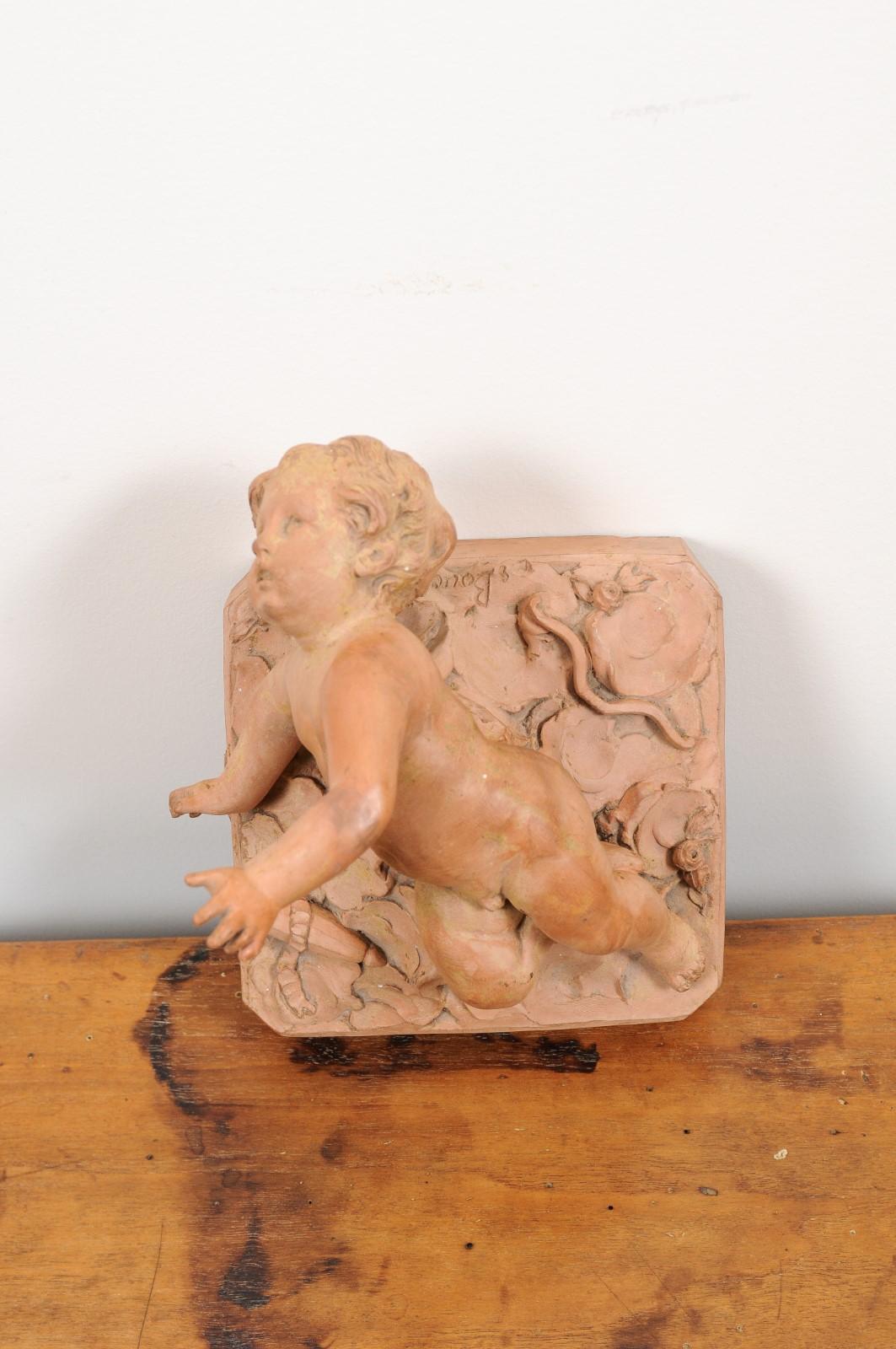 A French Empire period terracotta high relief cupid model from the early 19th century, signed. Created in France during the early years of the 19th century, this terracotta model features a high relief cupid, emerging from a cloudy background