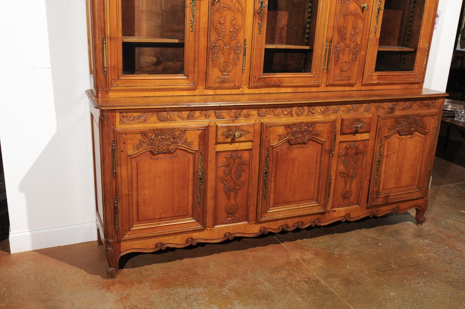 A French Restauration period walnut vitrine enfilade from the early 19th century, with bonnet-shaped cornice, foliage, agricultural tool motifs, glass doors and hidden panels. Born in France during the second decade of the 19th century, this walnut