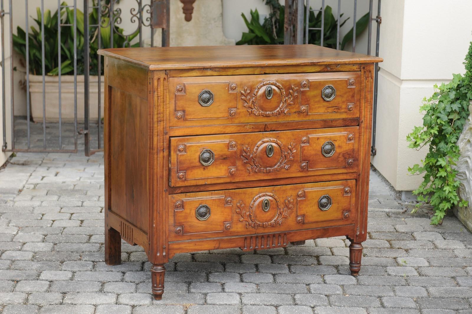 A French Restauration period walnut commode from the early 19th century, with three drawers, carved foliage and fluted accents. Born in France during the early years of the 19th century, this exquisite commode features a rectangular planked top