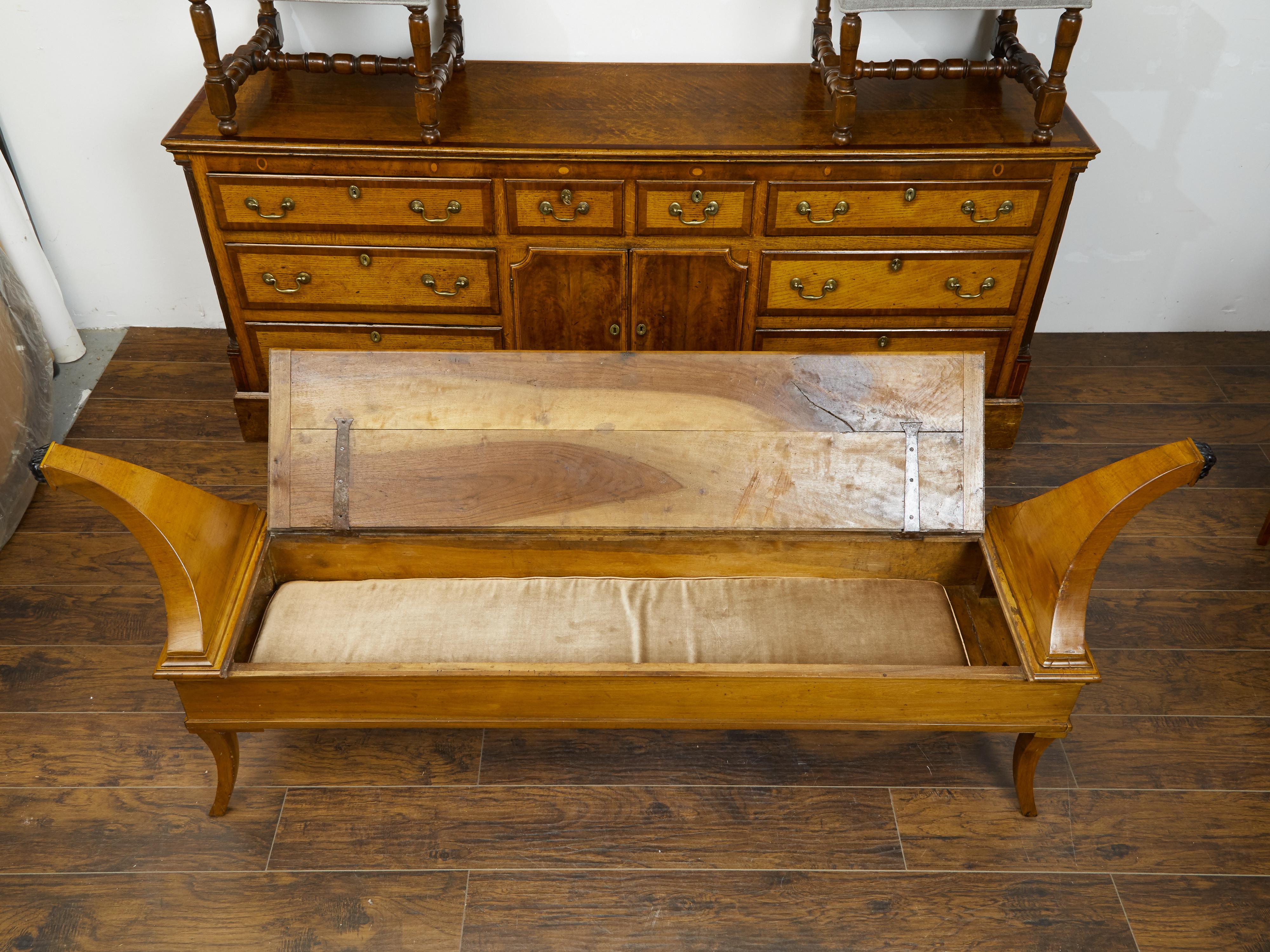 A French Restauration period walnut bench from the early 19th century, with lift-top seat, unusual out-scrolling arms and ebonized accents. Created in France during the first quarter of the 19th century, this Restauration bench captures our