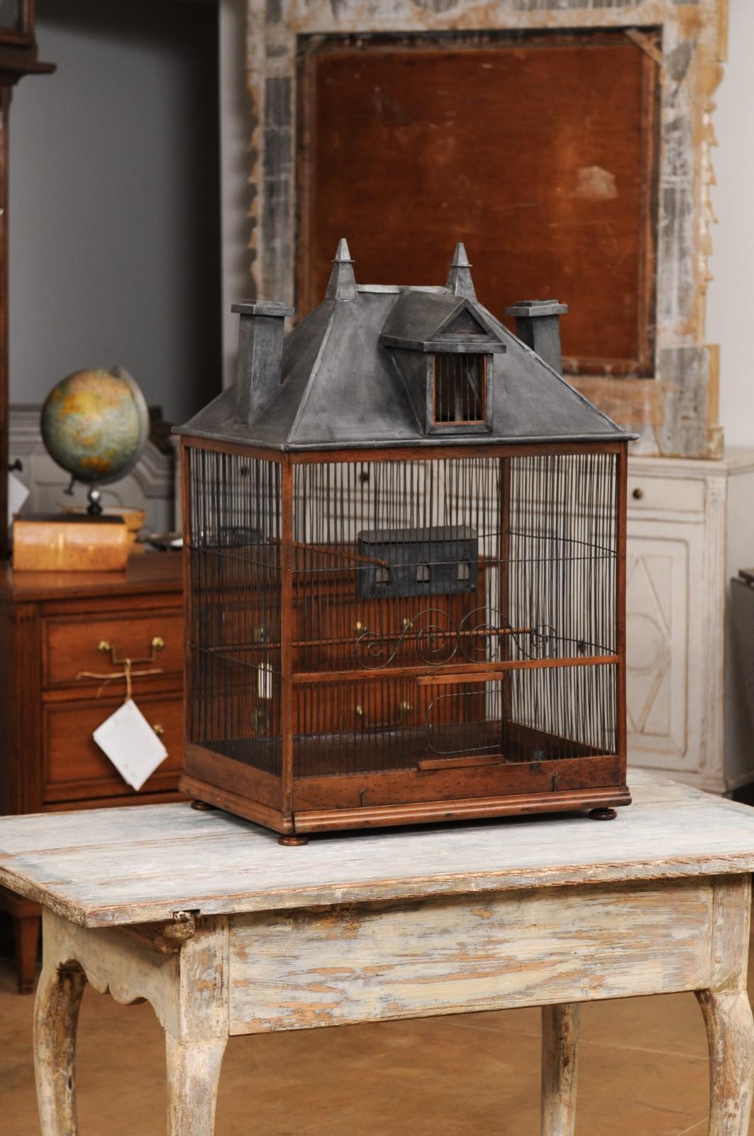 A French Restauration period rustic bird cage from the early 19th century, with tin slanted roof and chimneys. Created in France during the second quarter of the 19th century, this bird cage charms us with its rustic character and lovely décor.
