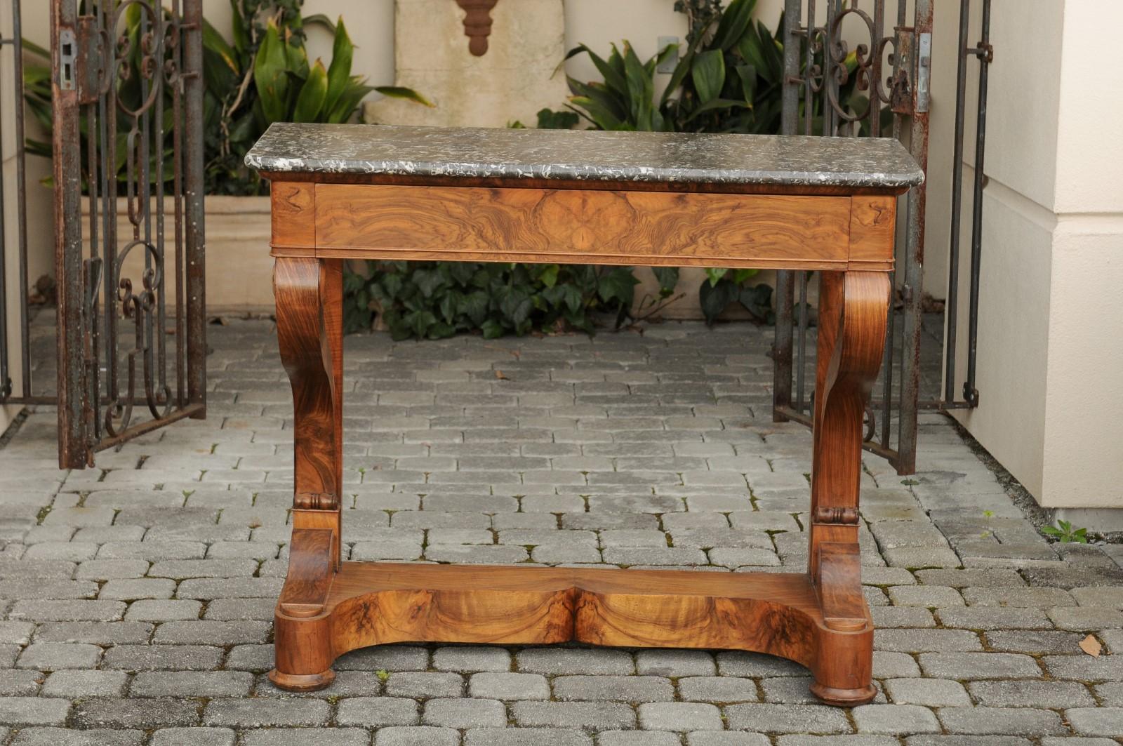 A French Louis-Philippe period walnut console table from the mid-19th century, with grey marble top and single drawer. Born in France during the reign of King Louis-Philippe, this exquisite walnut console table features a rectangular marble top with