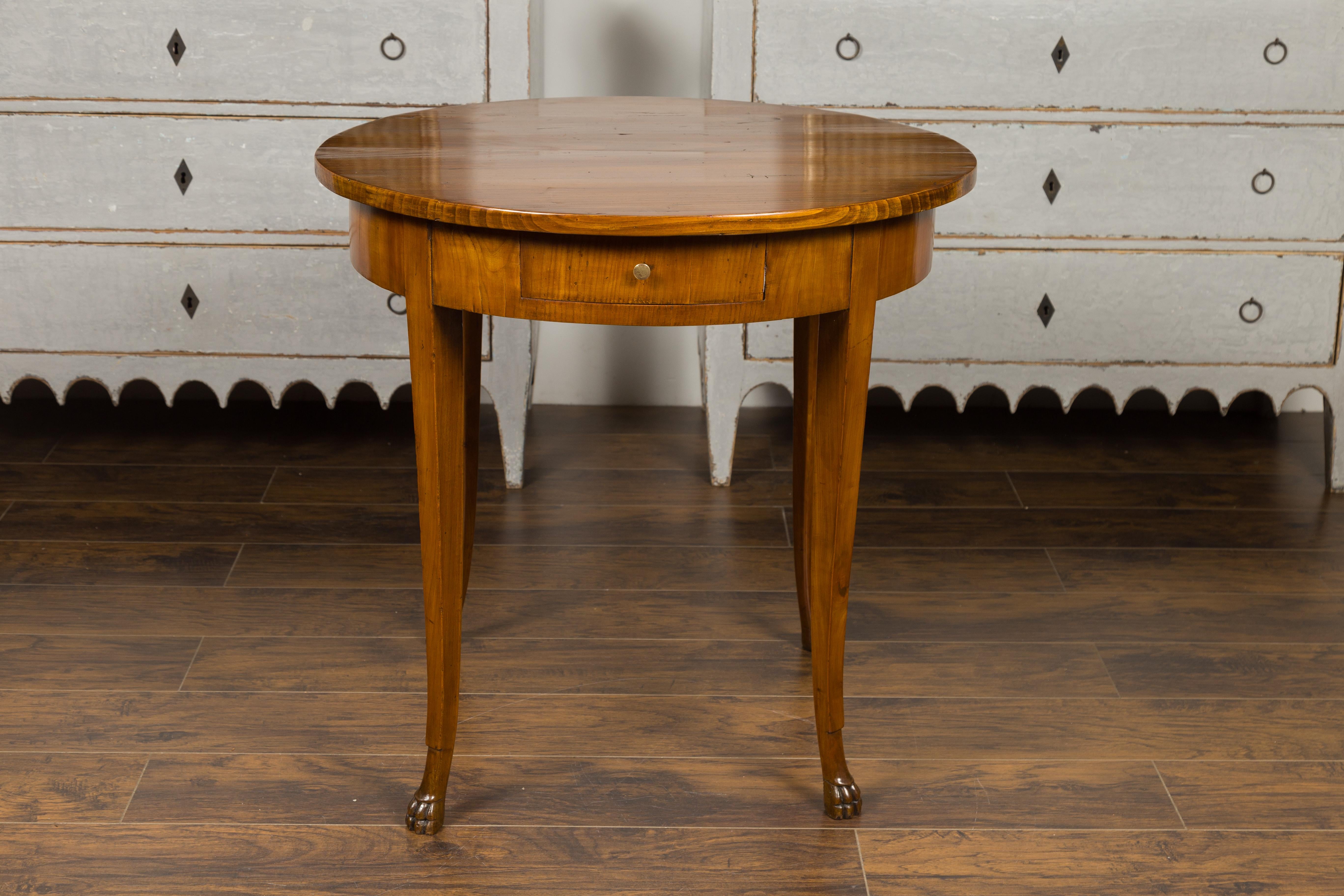 A French Louis-Philippe period walnut table from the mid-19th century, with single drawer and paw feet. Born in France during the reign of King Louis-Philippe, this walnut table features a circular top sitting above a single drawer fitted with a