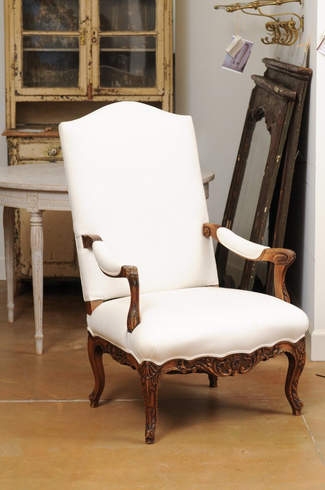 A French Louis XV style walnut fauteuil from the mid 19th century, with carved accents and newer upholstery. Created in France during the second quarter of the 19th century, this walnut armchair features a slanted camelback connected to two open