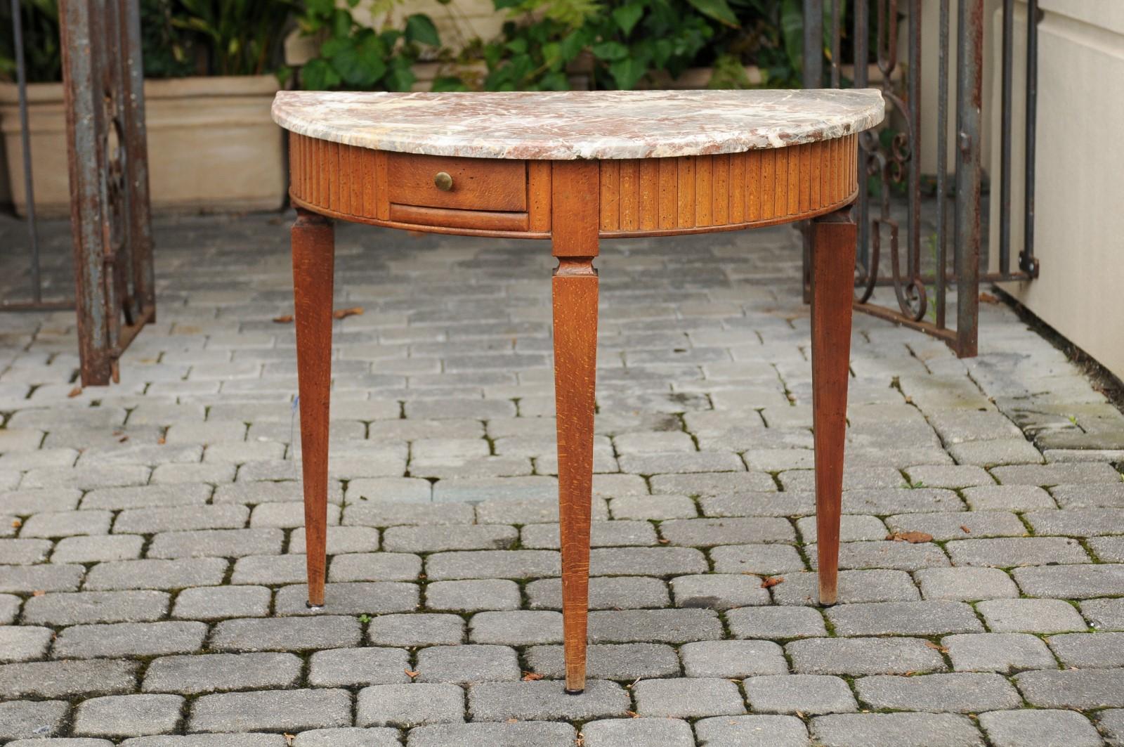 This French neoclassical style mid-19th century oak demilune console table features a half moon shaped top made of a lovely grey variegated marble top. The unique reeded wooden apron is decorated with a single asymmetrical drawer. This circa 1840